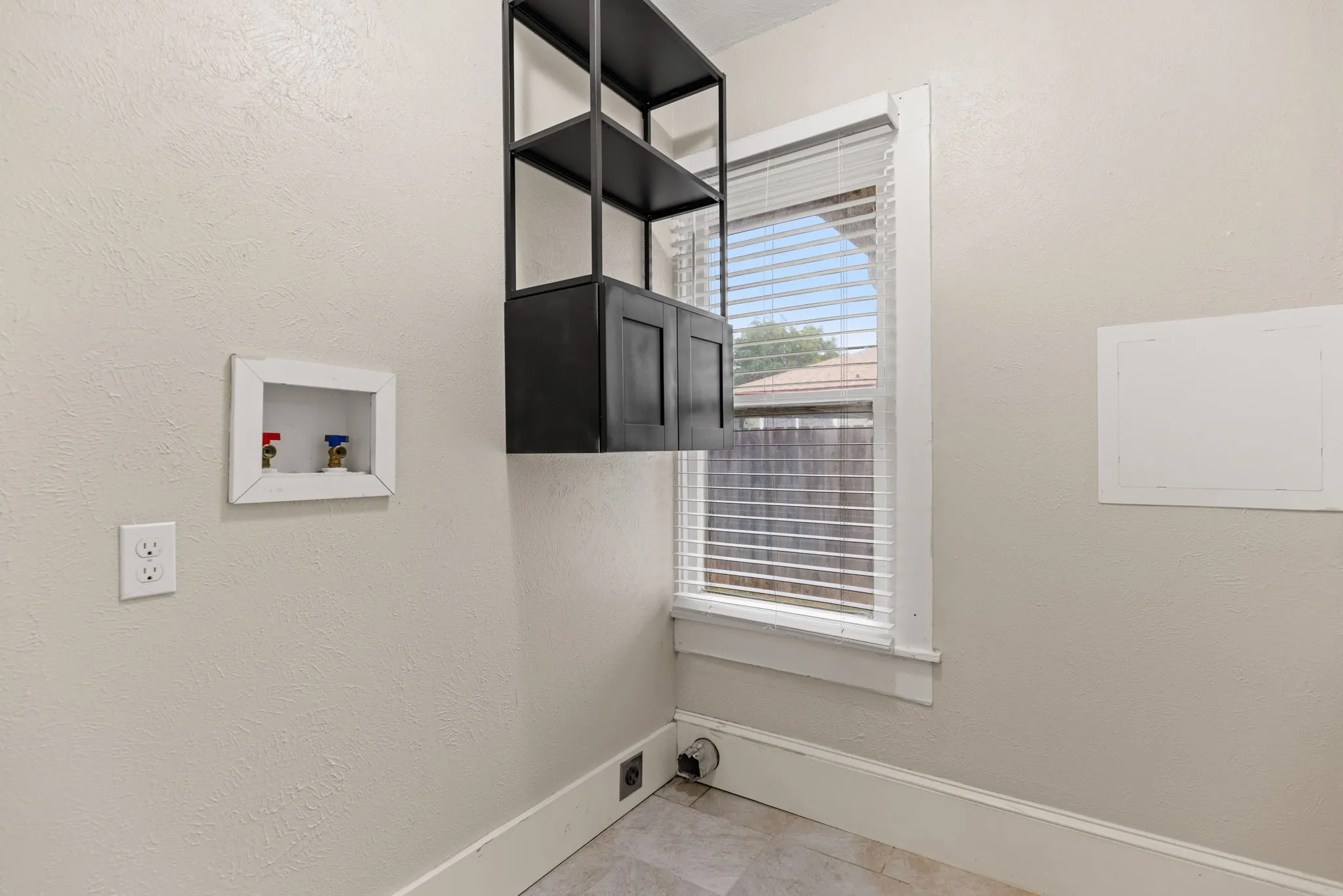 Dedicated utility space featuring a window with horizontal blinds, a utility hookup, and a wall-mounted shelving unit