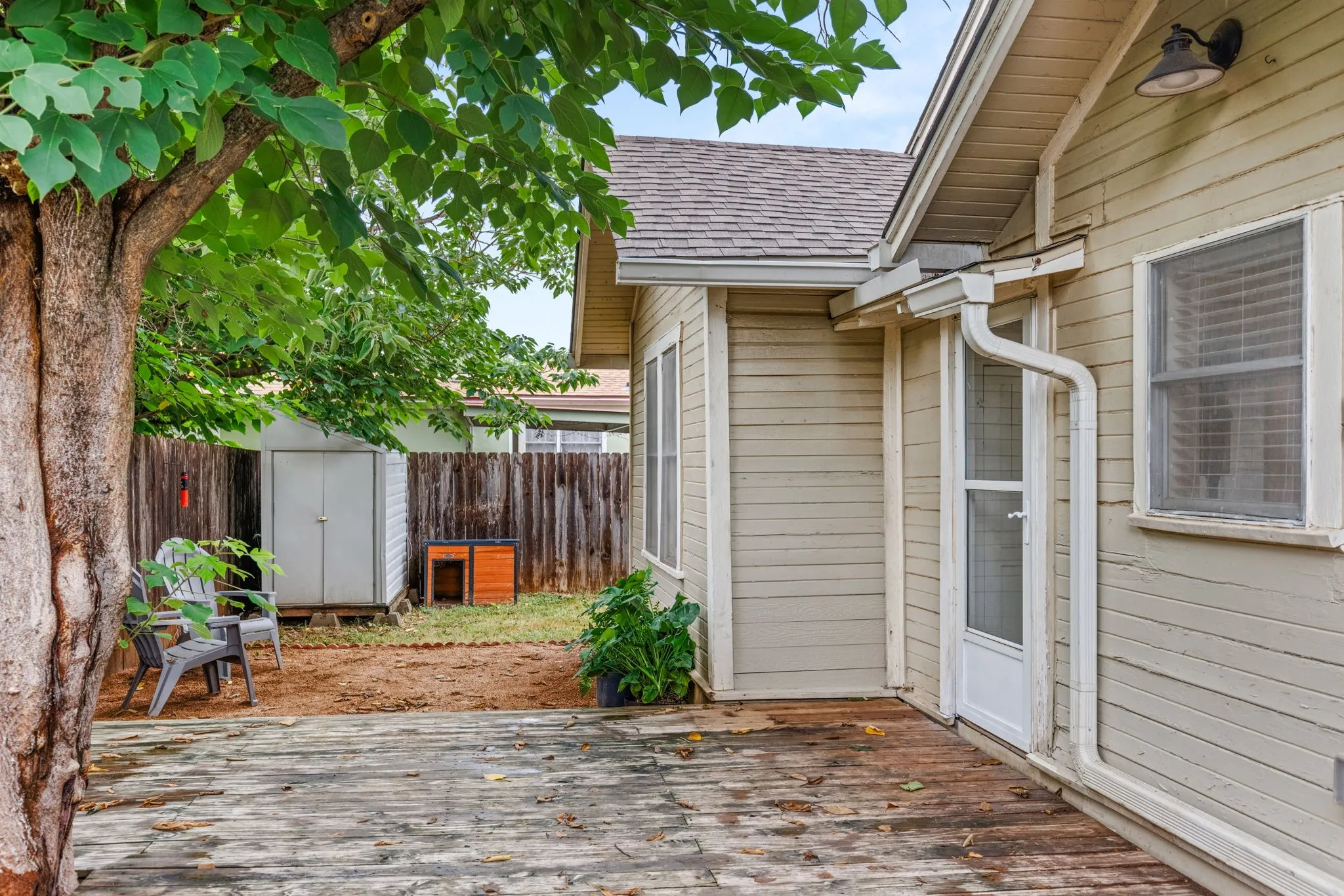 Backyard featuring a wooden deck, a mature shade tree, a white storage shed, and a privacy fence