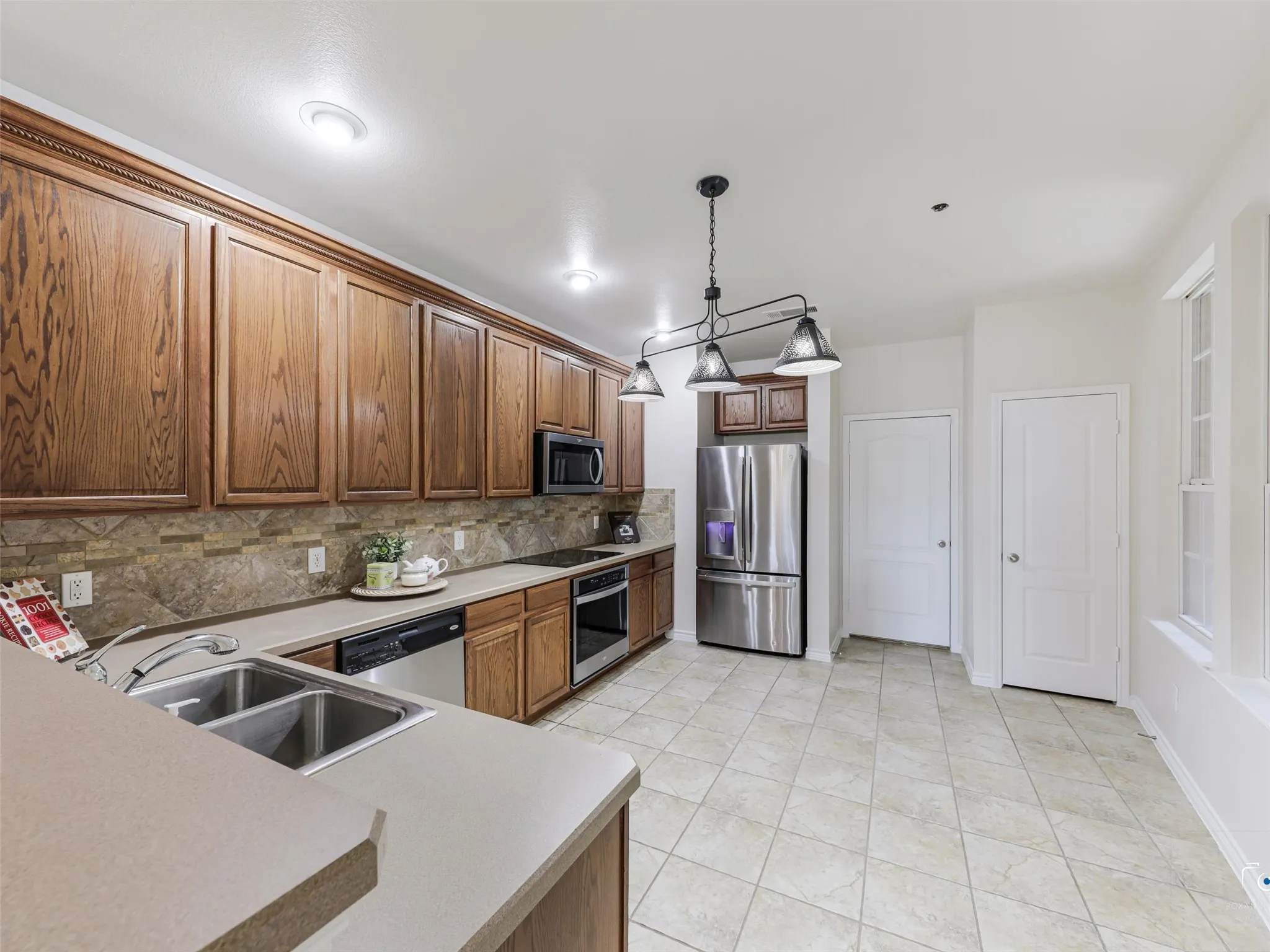 Kitchen featuring extensive wood cabinetry, stainless steel appliances, a dual basin sink, tile flooring, and a stone tile backsplash