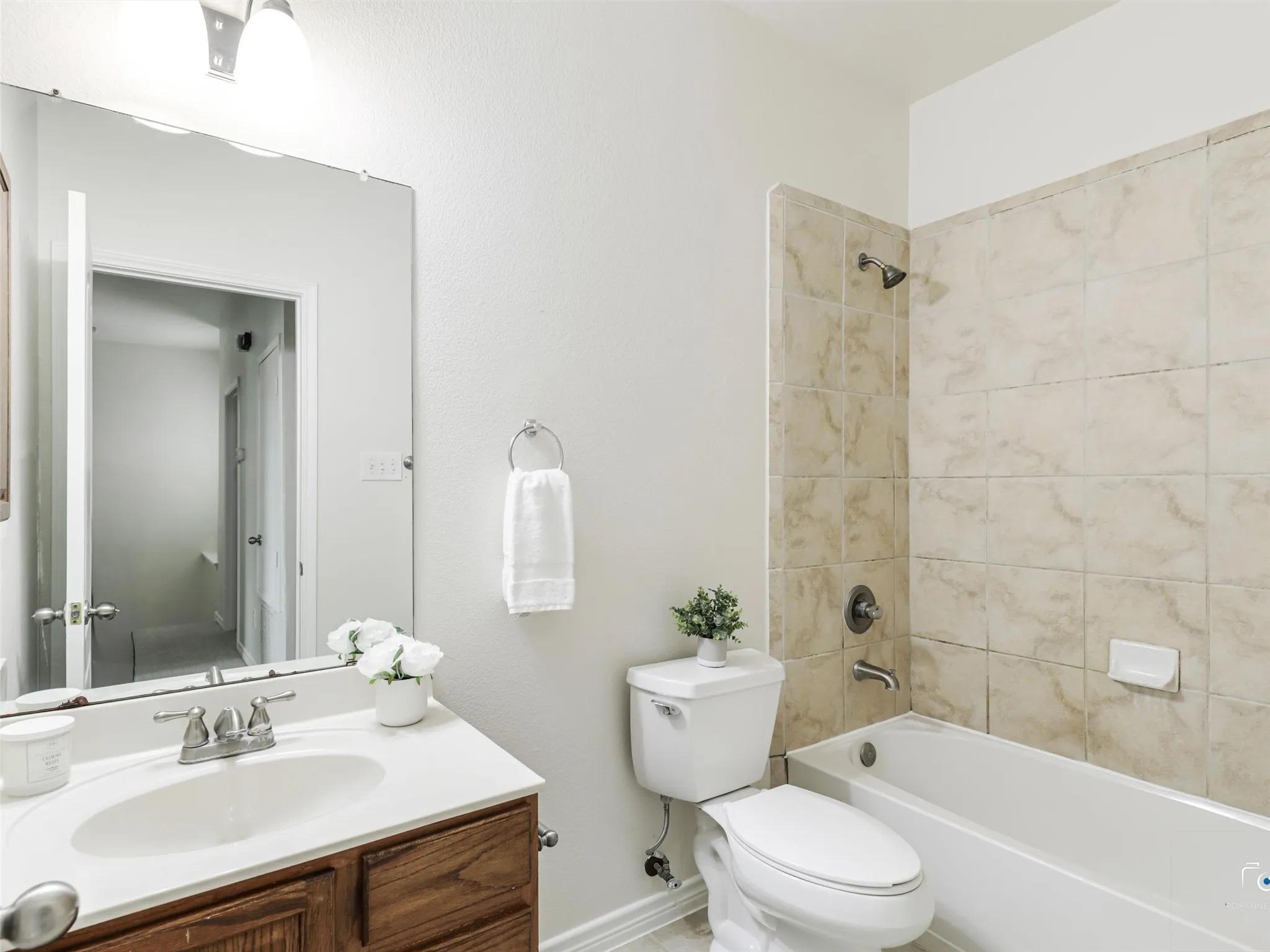 Full bathroom featuring a wood-finish vanity with an integrated sink, polished chrome hardware, a full-width mirror, and a tiled shower-over-tub combination with a matching polished chrome showerhead and faucet