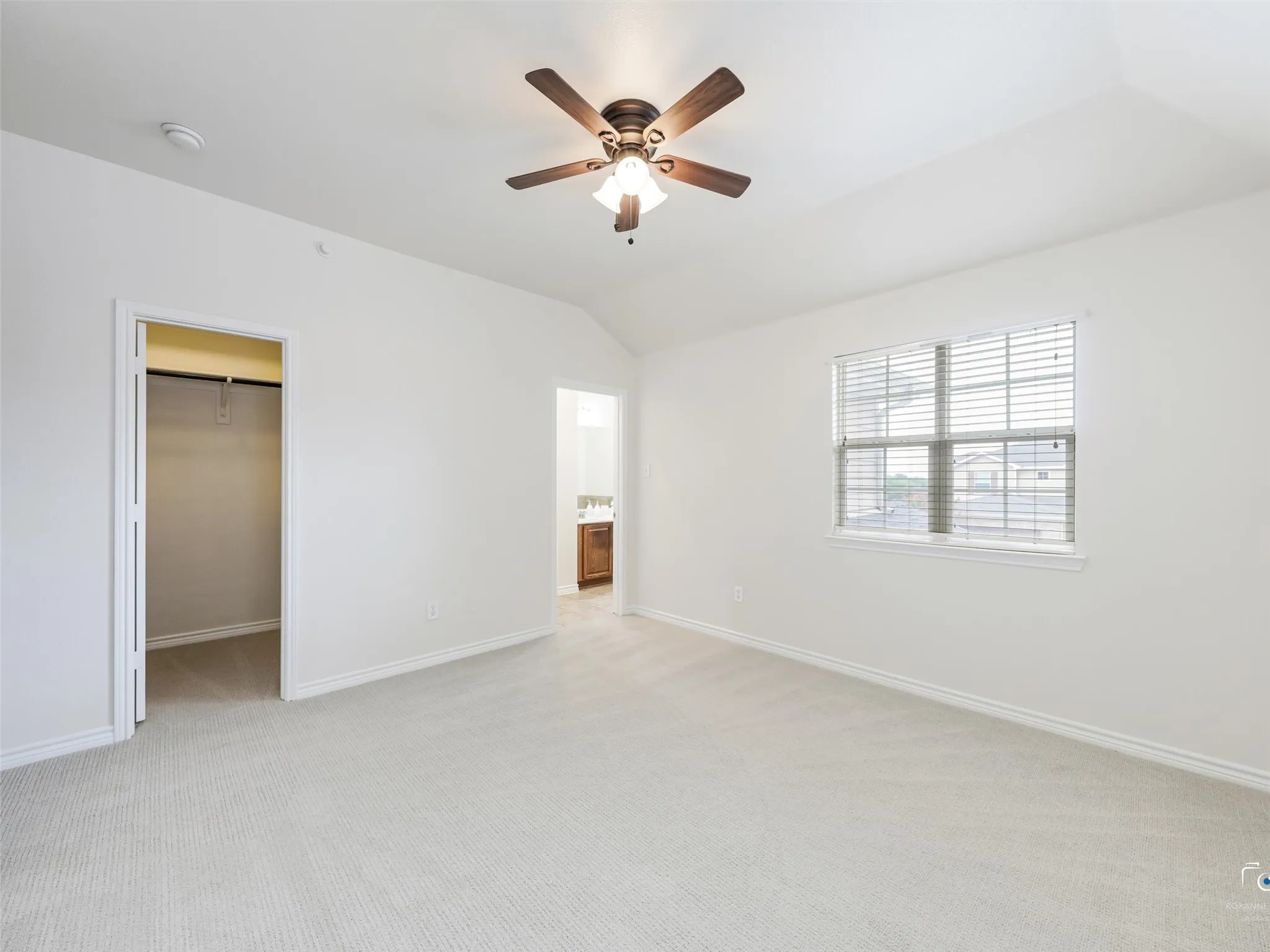 Spacious room featuring vaulted ceiling, ceiling fan with light fixture, light-toned carpeting, window with blinds, and an open closet