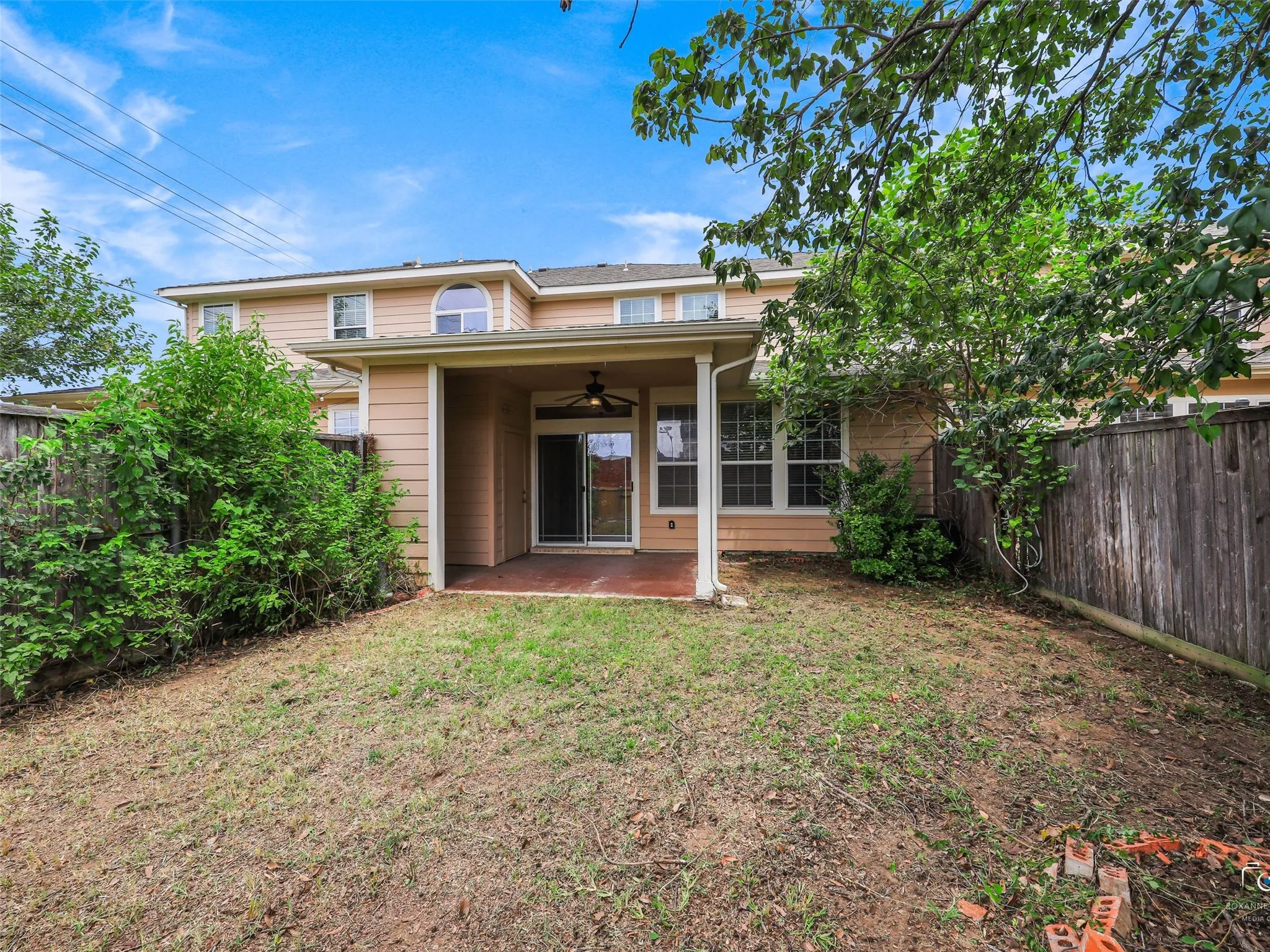 Rear exterior featuring a covered patio with a ceiling fan, sliding glass doors, and a partial privacy fence