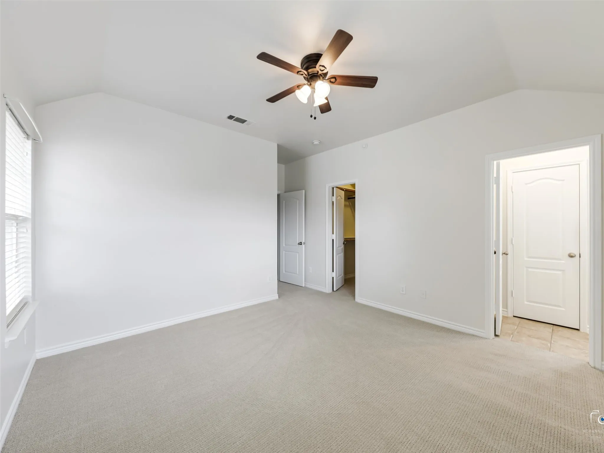 Vaulted ceiling room featuring light-toned carpet flooring, white walls, and a ceiling fan with integrated lighting