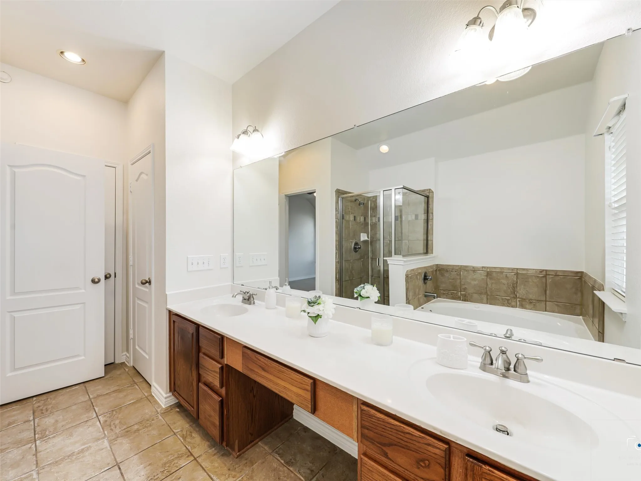 Bathroom featuring a dual vanity with wood cabinetry and white countertops, a large frameless mirror, and a combination shower and bathtub with tile surround