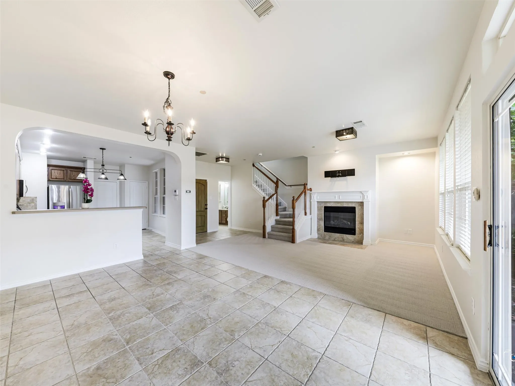 Spacious living area featuring tile flooring, a fireplace with stone surround, staircase with wood banister, and an arched pass-through to the kitchen with a breakfast bar