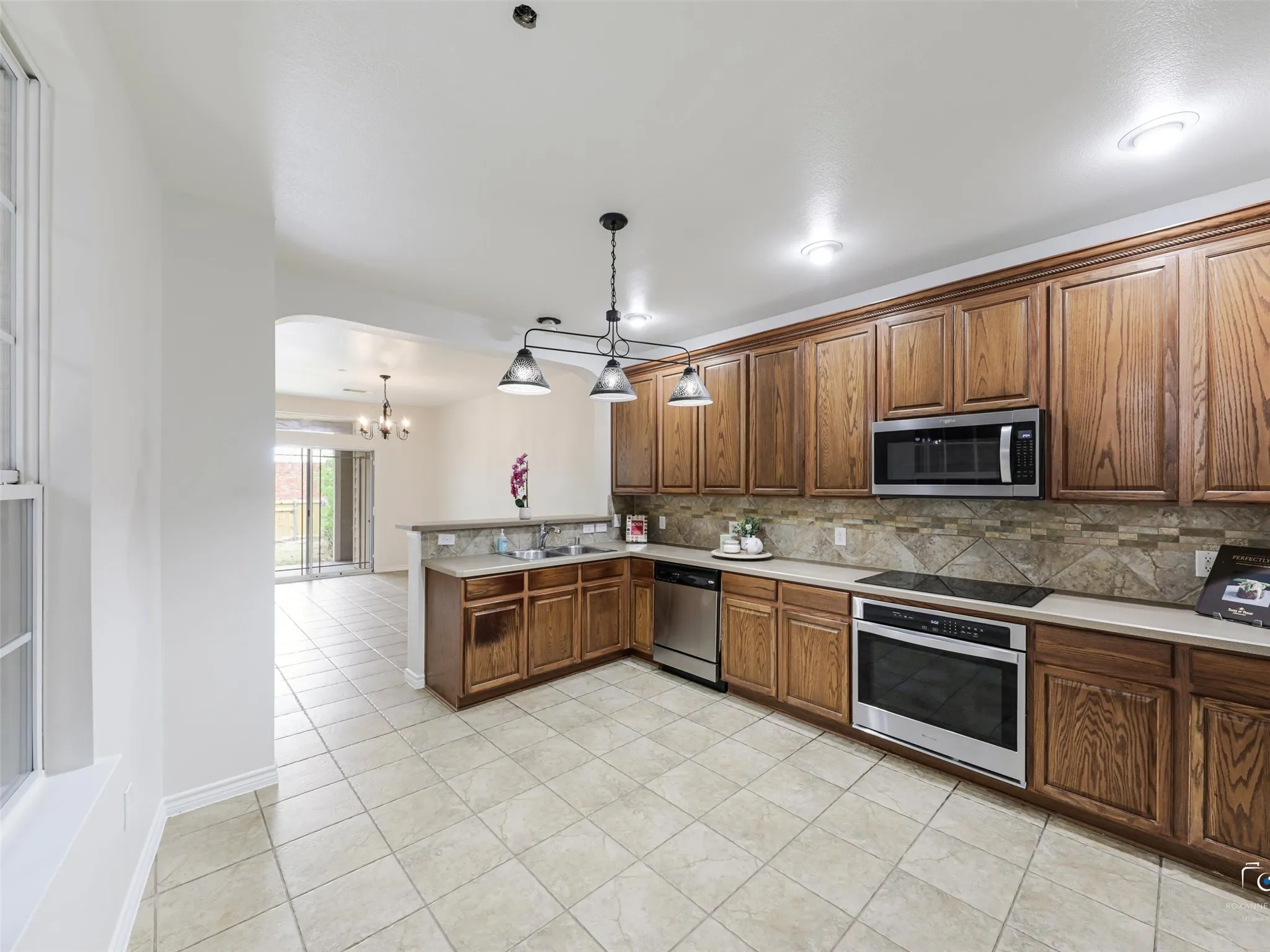 Kitchen featuring wood cabinetry, stainless steel appliances, mosaic tile backsplash, a bar-height counter, and tile flooring