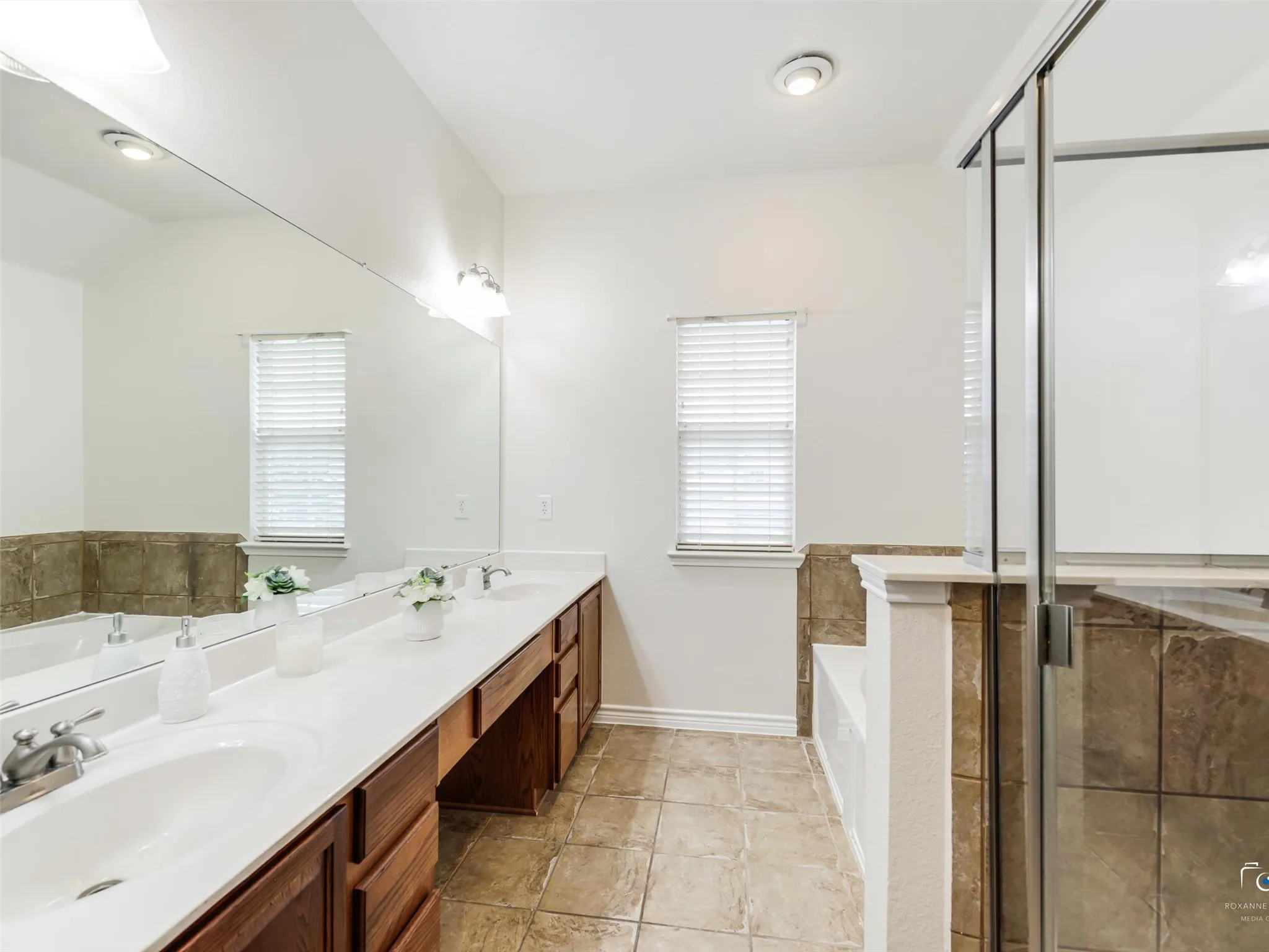 Bathroom featuring a dual vanity with white countertops, wood-finish cabinetry, and an expansive mirror