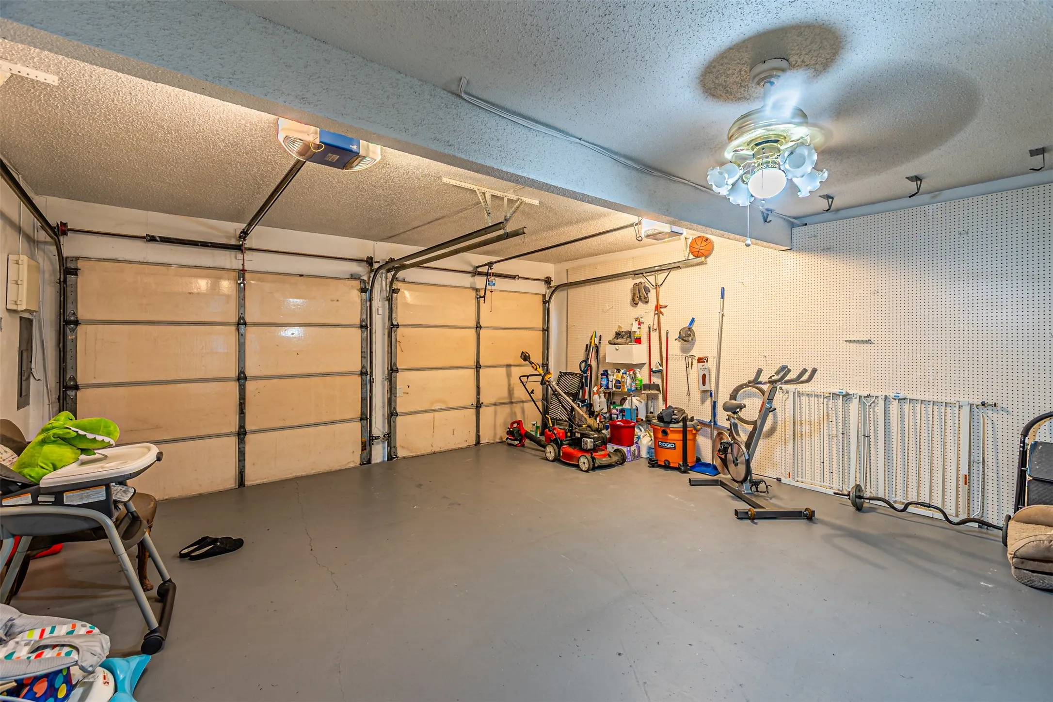 Two-car garage featuring segmented overhead doors, grey painted flooring, and a ceiling-mounted fan with light fixture