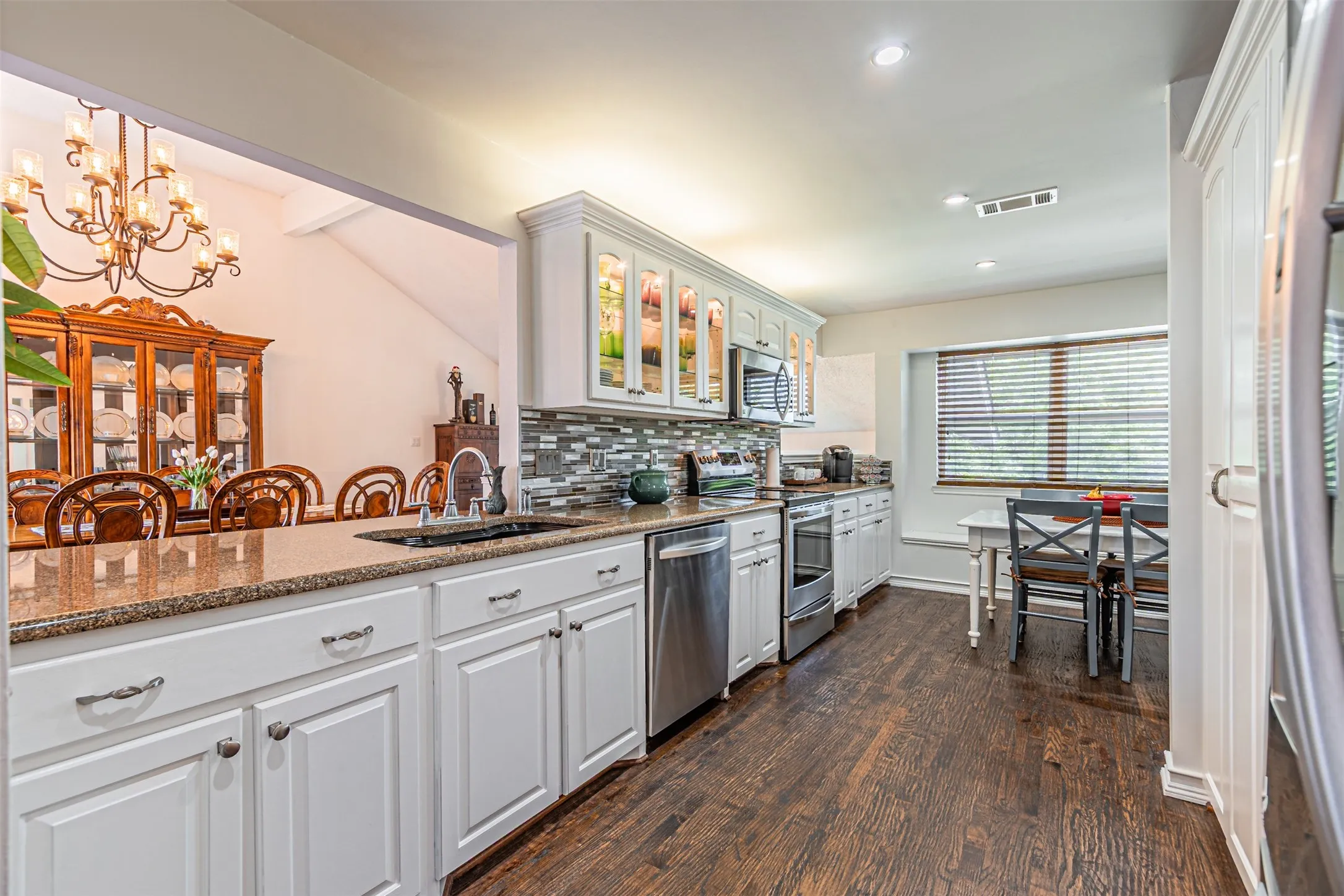 Kitchen featuring white cabinetry, granite countertops, stainless steel appliances, a tile backsplash, and wood-finish flooring