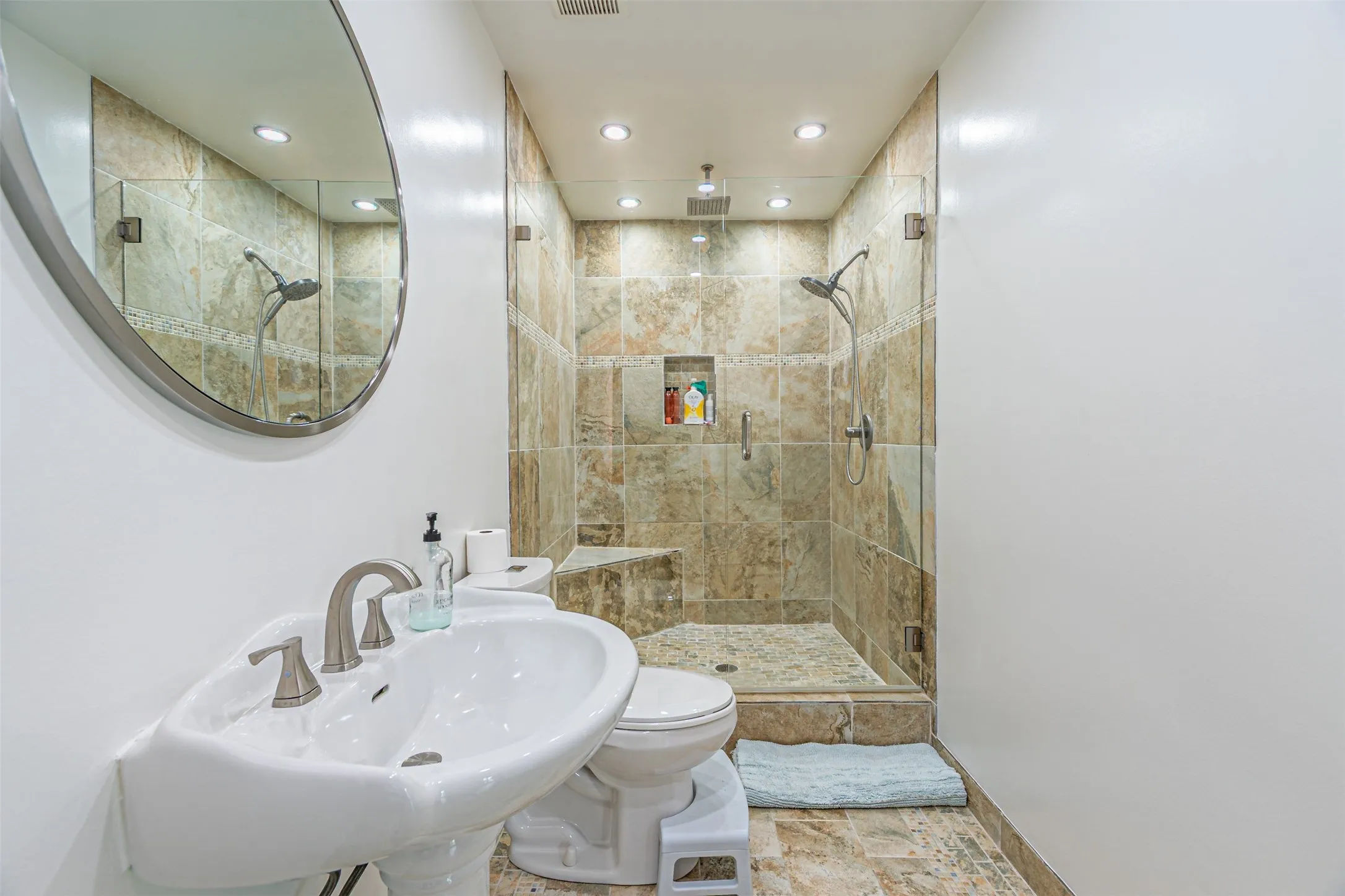 Pedestal sink with brushed nickel faucet, oval mirror, and recessed lighting