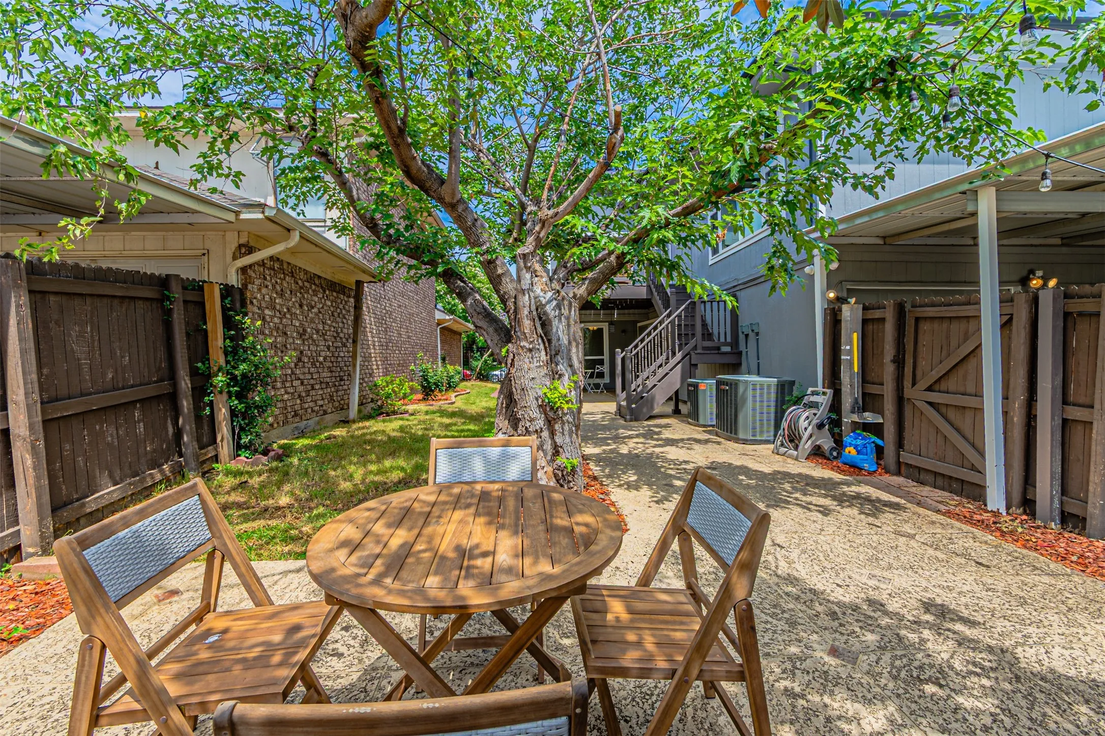 Paved outdoor area featuring mature trees, a multi-level structure with exterior stairs, and a covered patio area