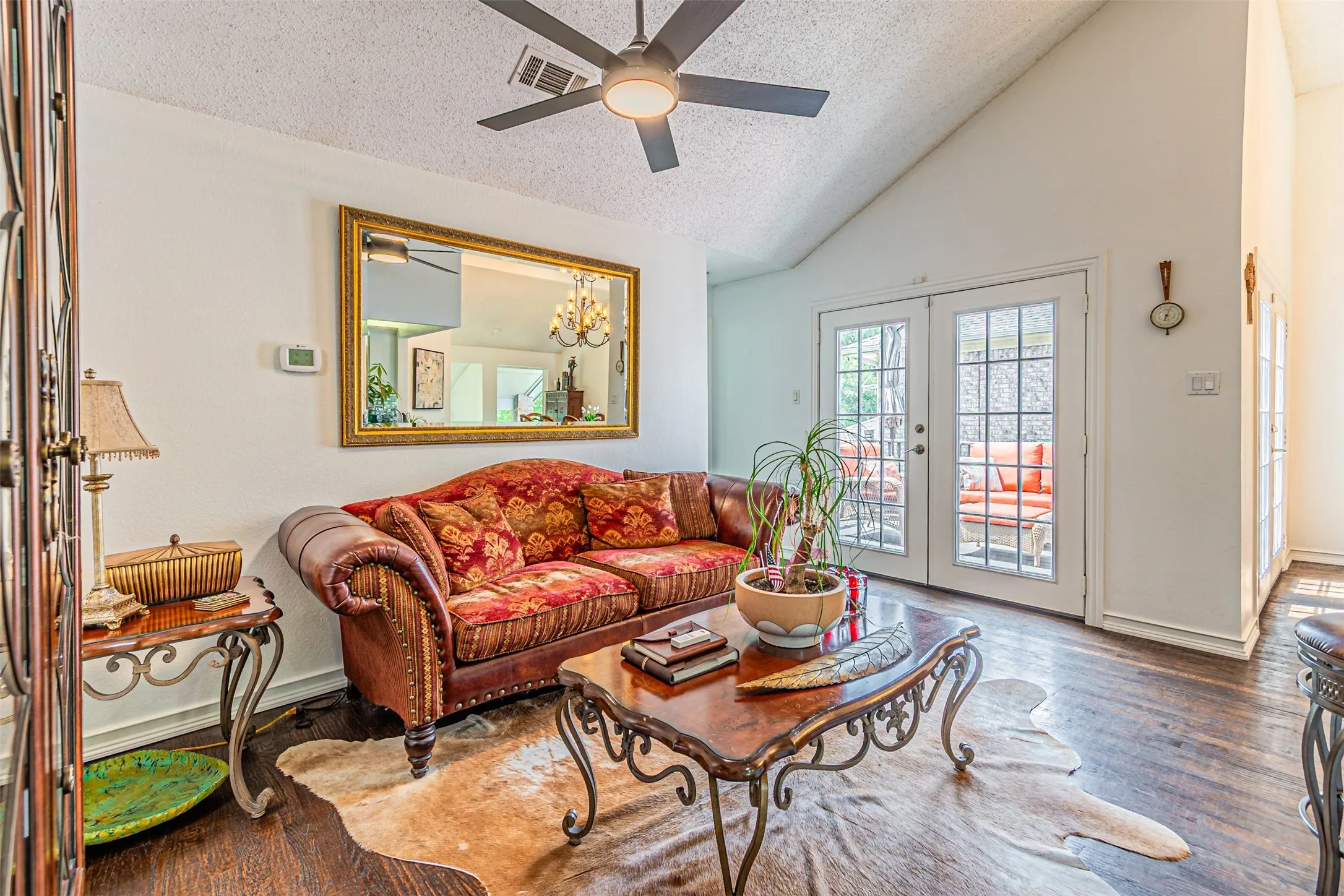 Vaulted ceiling living area featuring wood-finish flooring, a ceiling fan, and French doors