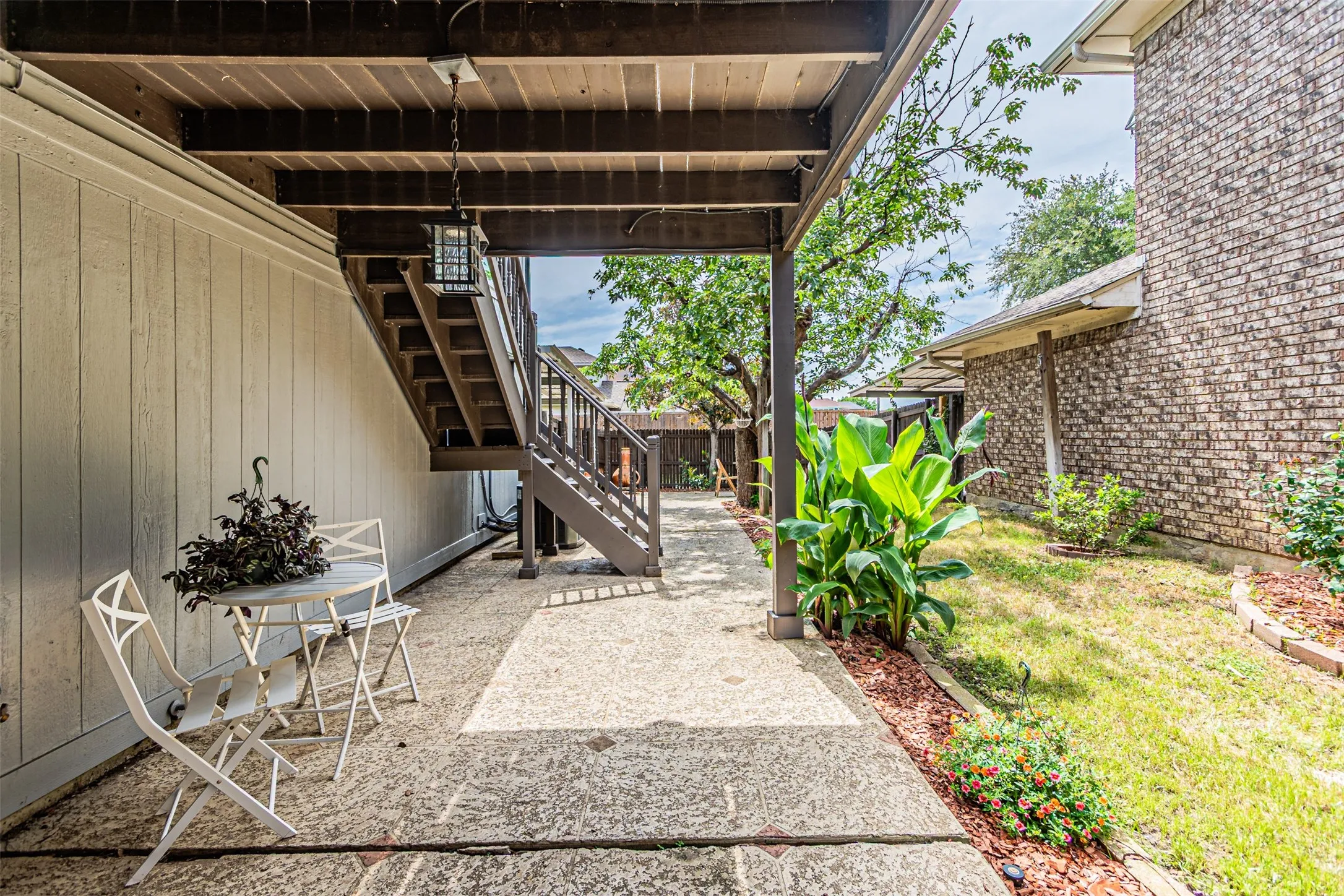Covered patio with a concrete surface, featuring a wood-tone staircase and an exterior wall with vertical siding