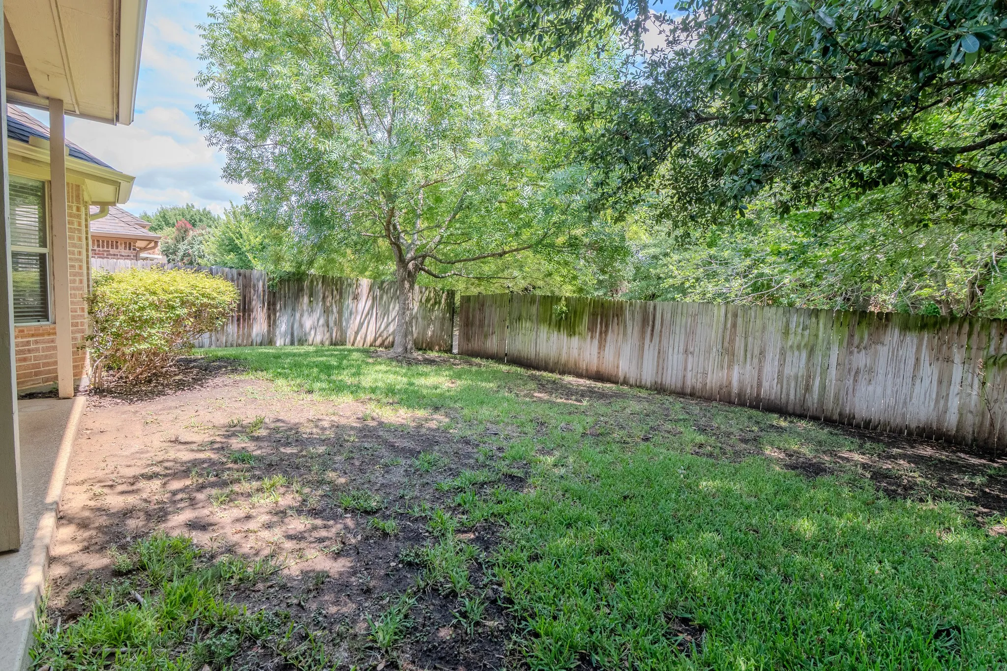 Expansive backyard featuring a partial patio, mature trees, and a perimeter privacy fence