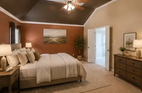 VIRTUALLY STAGED.  Primary bedroom featuring warm terracotta accent walls, a tray ceiling with ceiling fan and integrated lighting, neutral bedding, wood-finish nightstands with table lamps, a wood-finish dresser, and neutral area rug