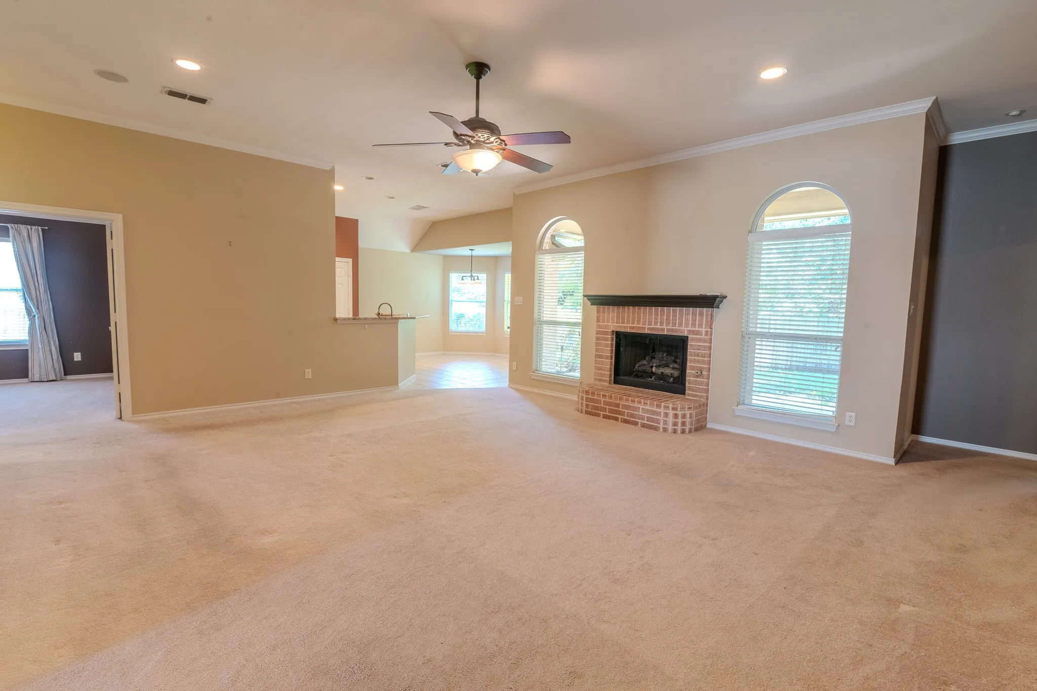 Spacious living area featuring a brick fireplace with a dark mantel, arched windows, recessed lighting, and a ceiling fan