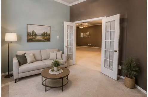 VIRTUALLY STAGED. Elegant living room showcasing neutral wood-finish flooring, a neutral upholstered sofa, and a round wood-finish center table