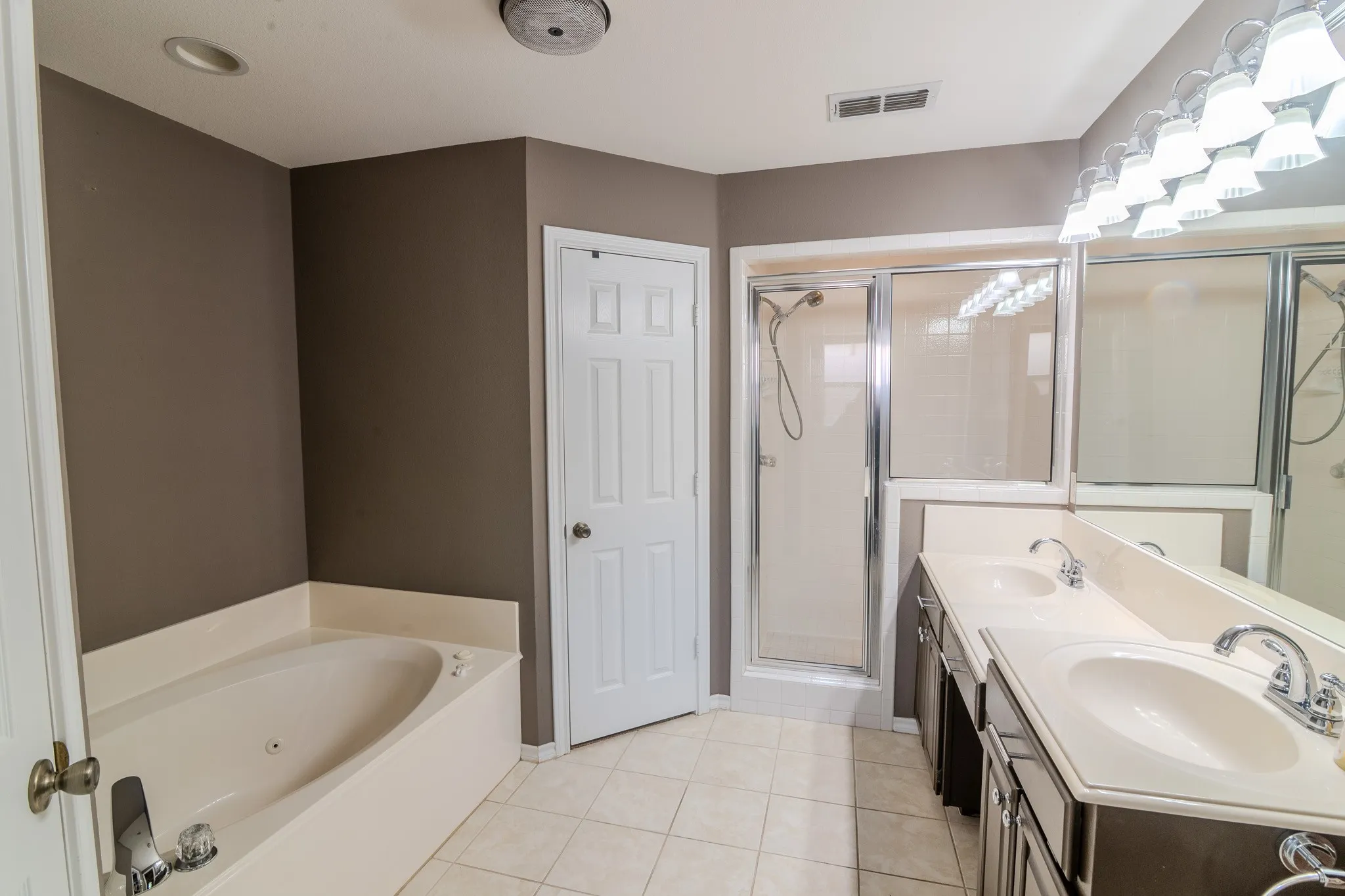 Bathroom featuring a built-in jetted tub, enclosed shower with sliding glass doors, double vanity with integrated sinks, chrome fixtures, and tiled flooring