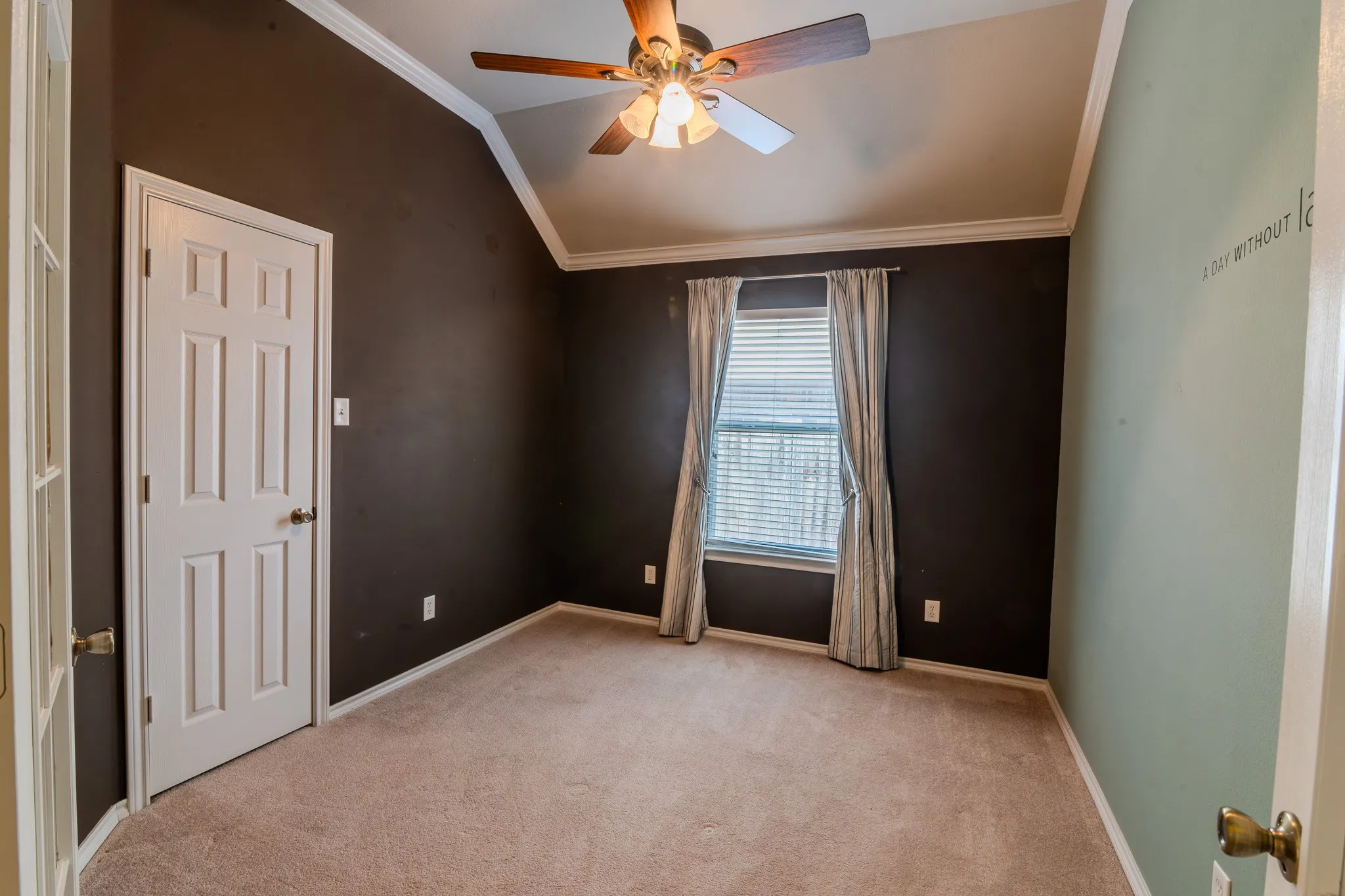 Carpeted room featuring a ceiling fan with light fixture, vaulted ceiling, crown molding, and a window with blinds