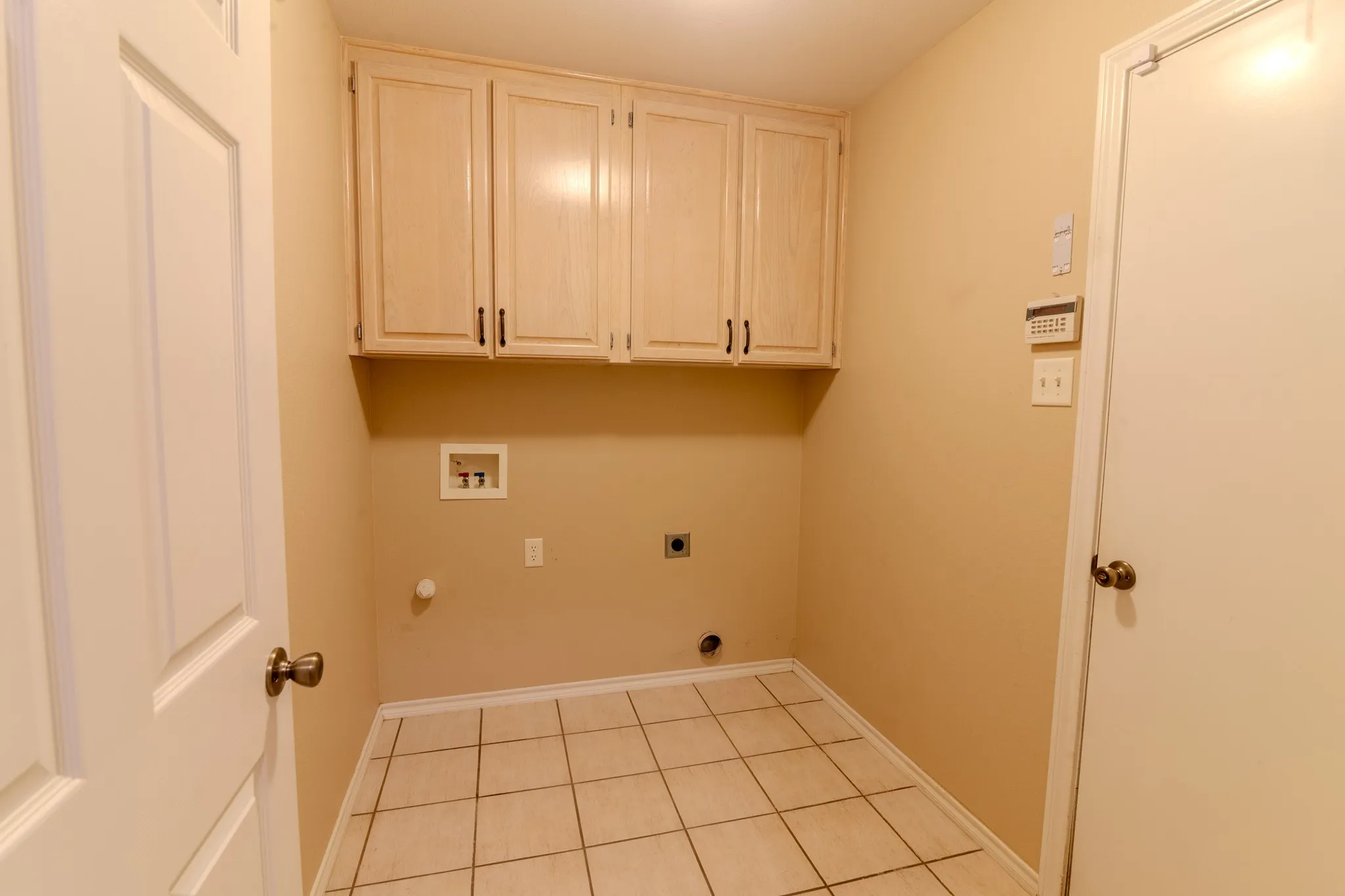 Laundry space featuring light-toned cabinetry with dark hardware, square tile flooring, and light beige wall paint