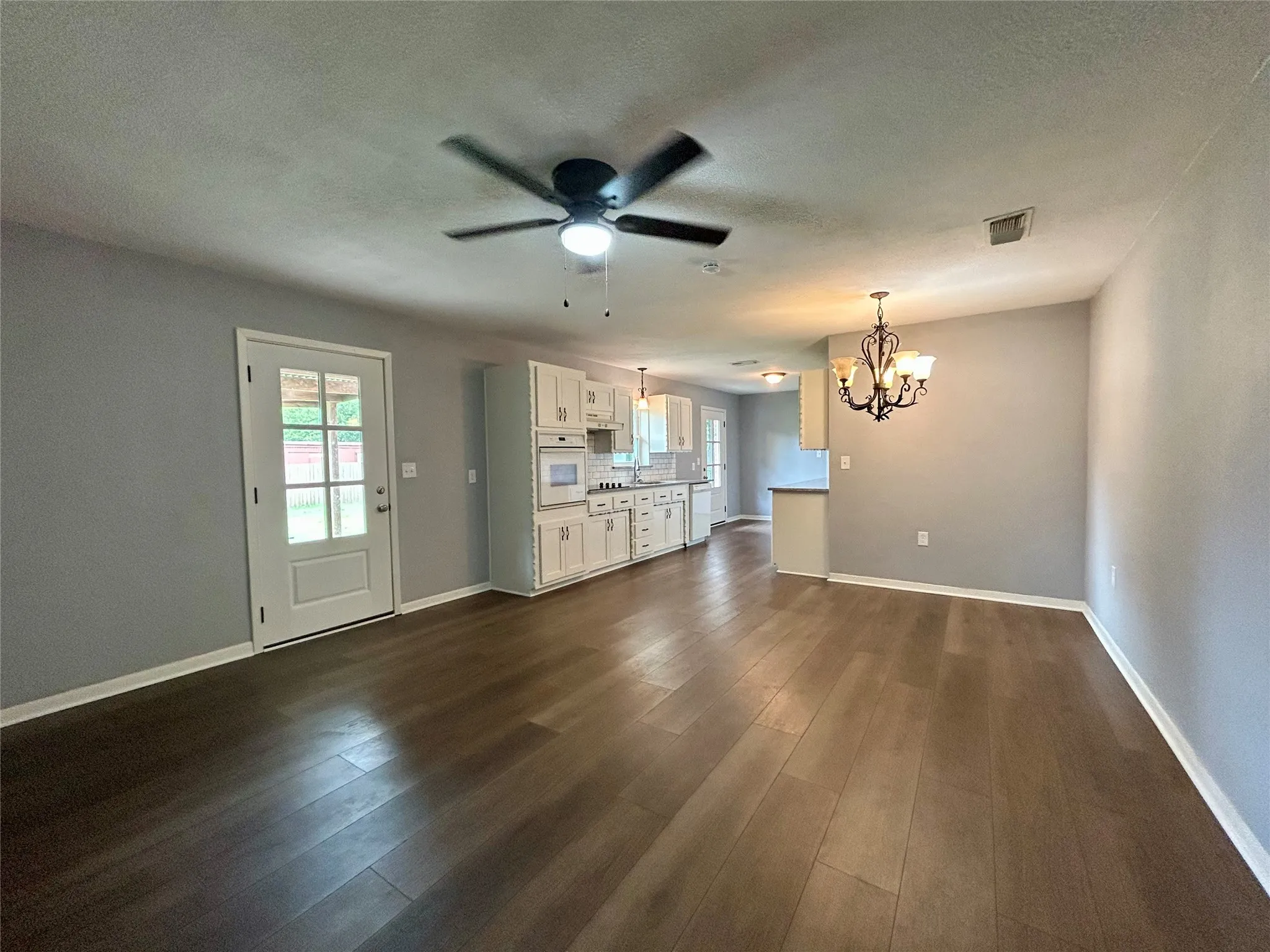 Spacious living area featuring wood-finish flooring, a ceiling fan, and a glass-paned door