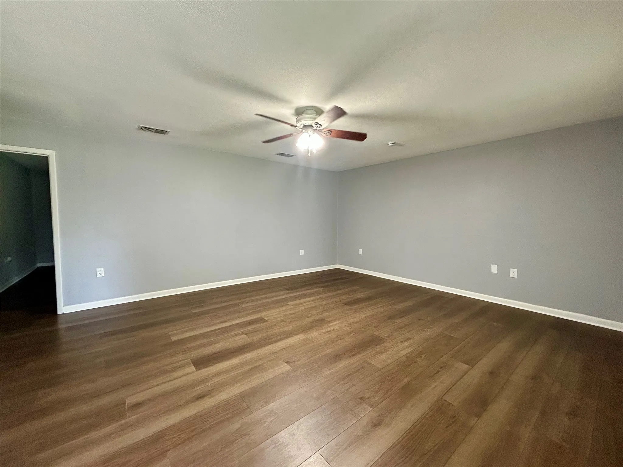 Spacious room featuring wood-finish flooring, light gray walls, white baseboards, and a ceiling fan with integrated lighting