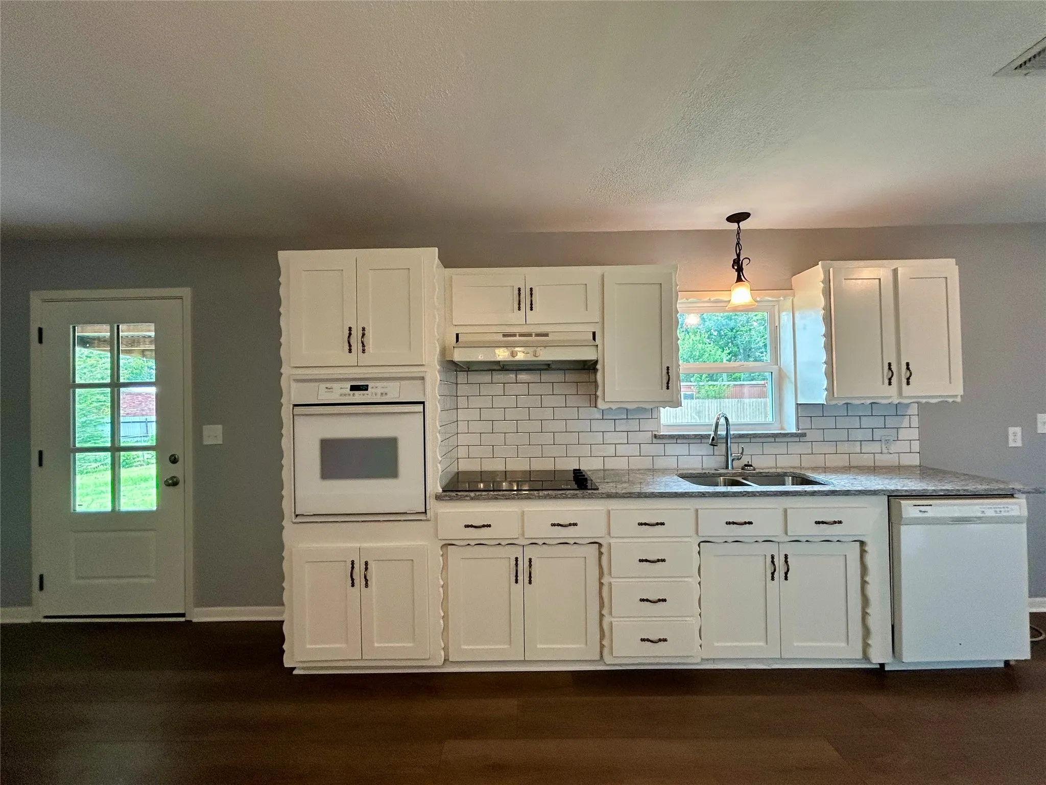 Kitchen featuring white cabinetry, subway tile backsplash, built-in oven, integrated dishwasher, and wood-finish flooring
