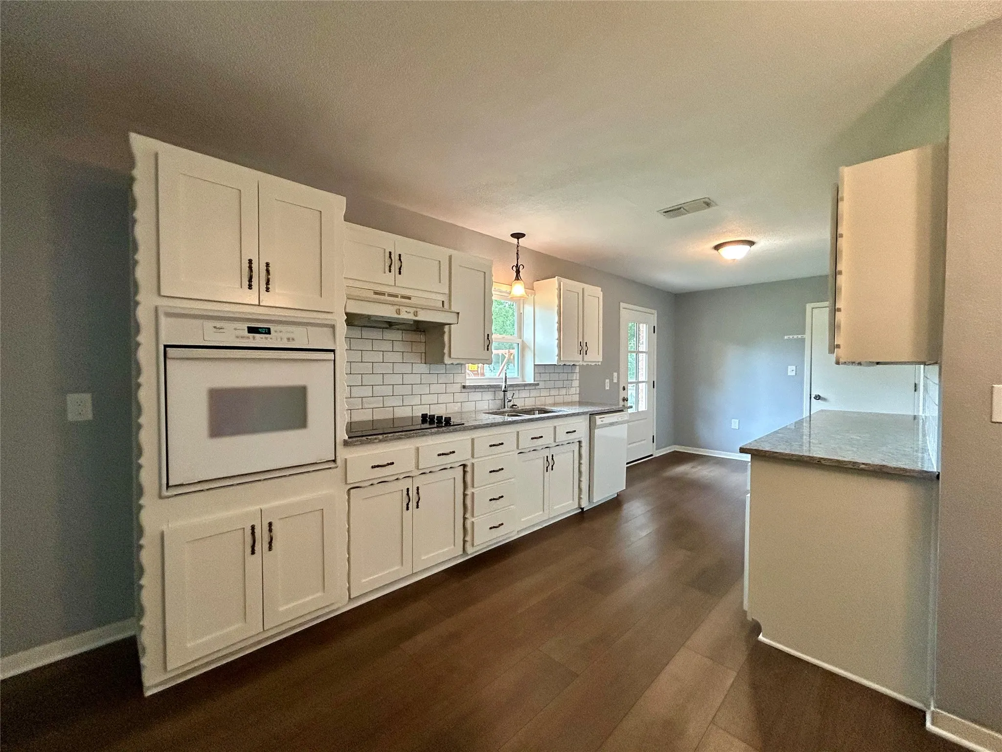 Kitchen featuring wood-finish flooring, white cabinetry, a built-in oven, subway tile backsplash, and stone countertops