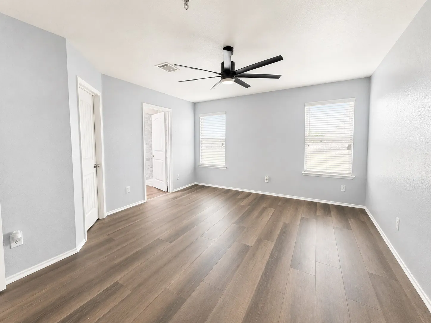 Spacious room featuring wood-finish flooring, light gray walls, white trim, and a contemporary black ceiling fan with integrated lighting
