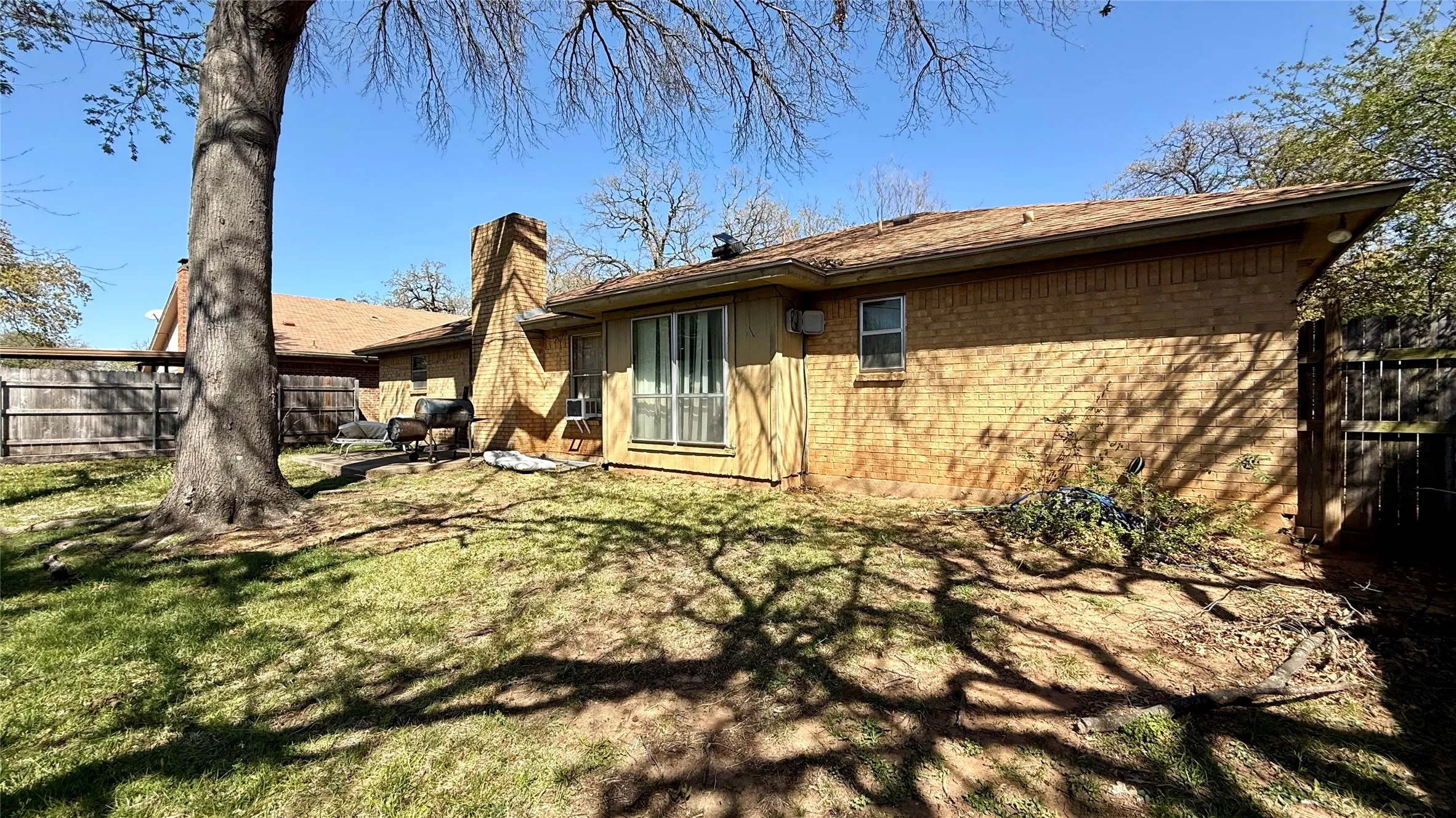 Expansive backyard featuring a mature tree, a full brick exterior, a substantial brick chimney, a wood fence, and a sliding glass door