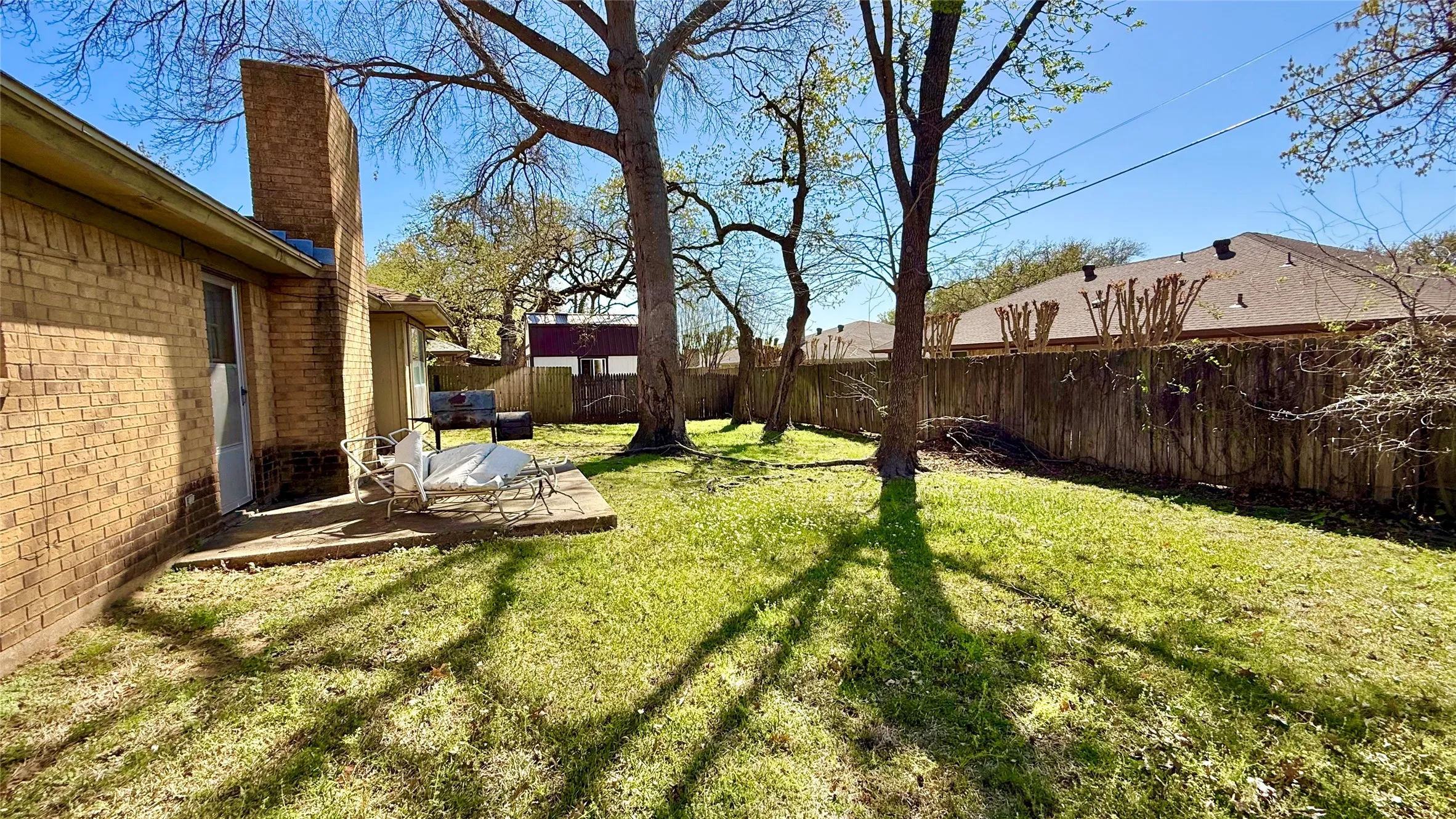 Expansive backyard featuring mature trees, a wood privacy fence, and a concrete patio