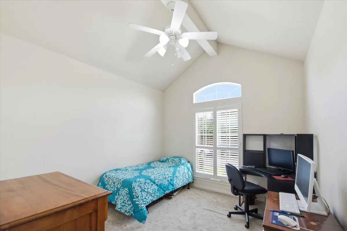 Vaulted ceiling bedroom featuring a ceiling fan, arched transom window, plantation shutters, and light-tone carpet flooring