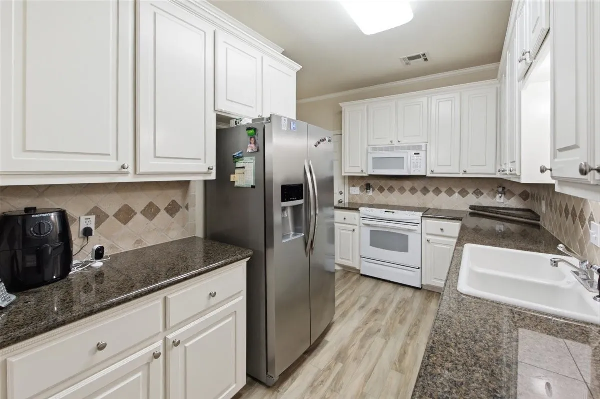 Bright kitchen featuring white cabinetry, dark granite countertops, and a tiled backsplash with diamond accents