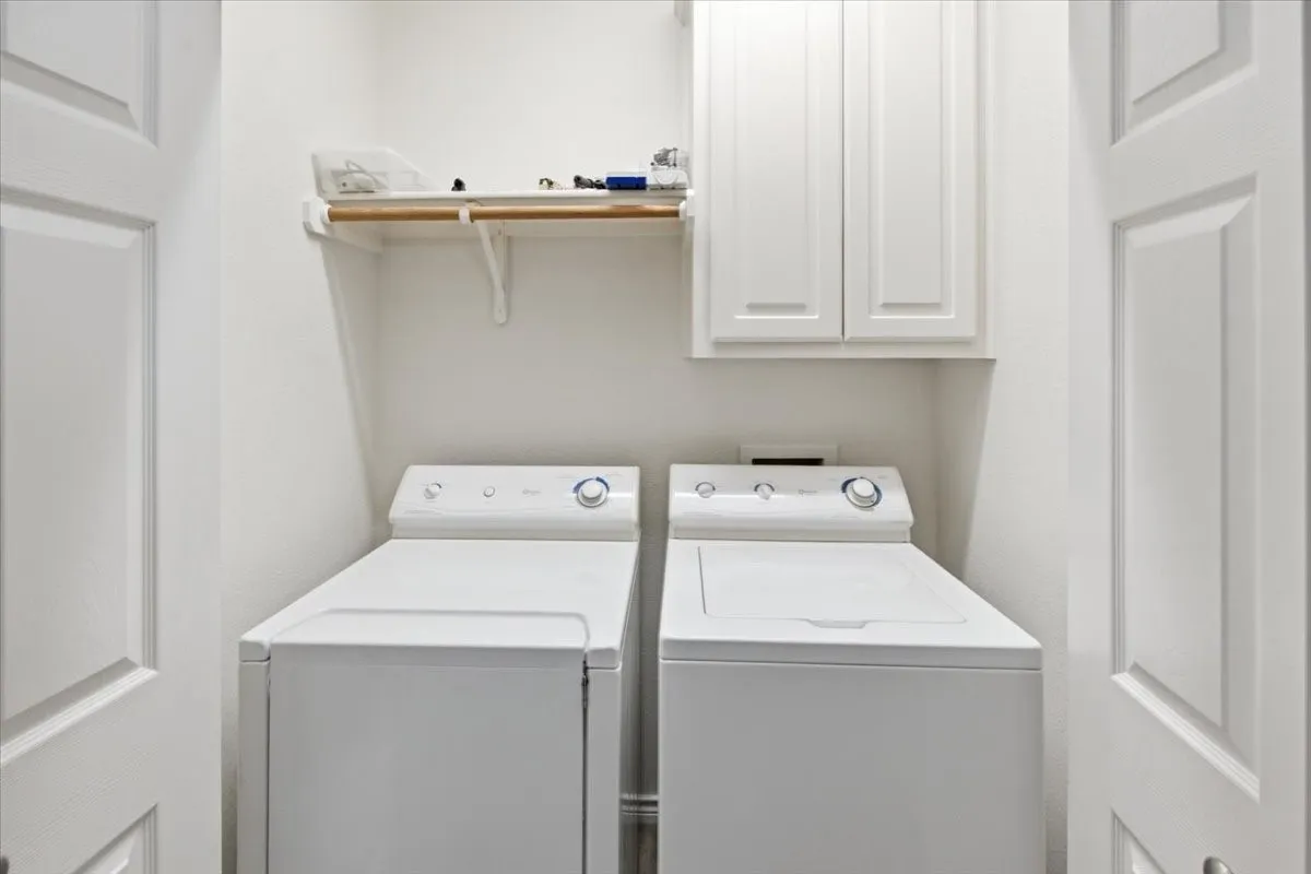 Dedicated laundry area featuring a white shaker-style wall cabinet, a wall-mounted wood shelf, and panel doors