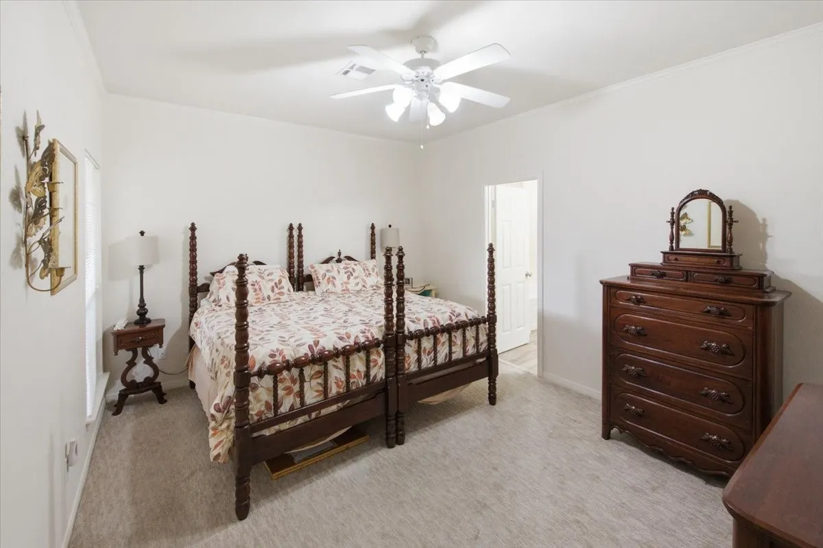 Carpeted primary bedroom with a ceiling fan, white walls, and crown molding