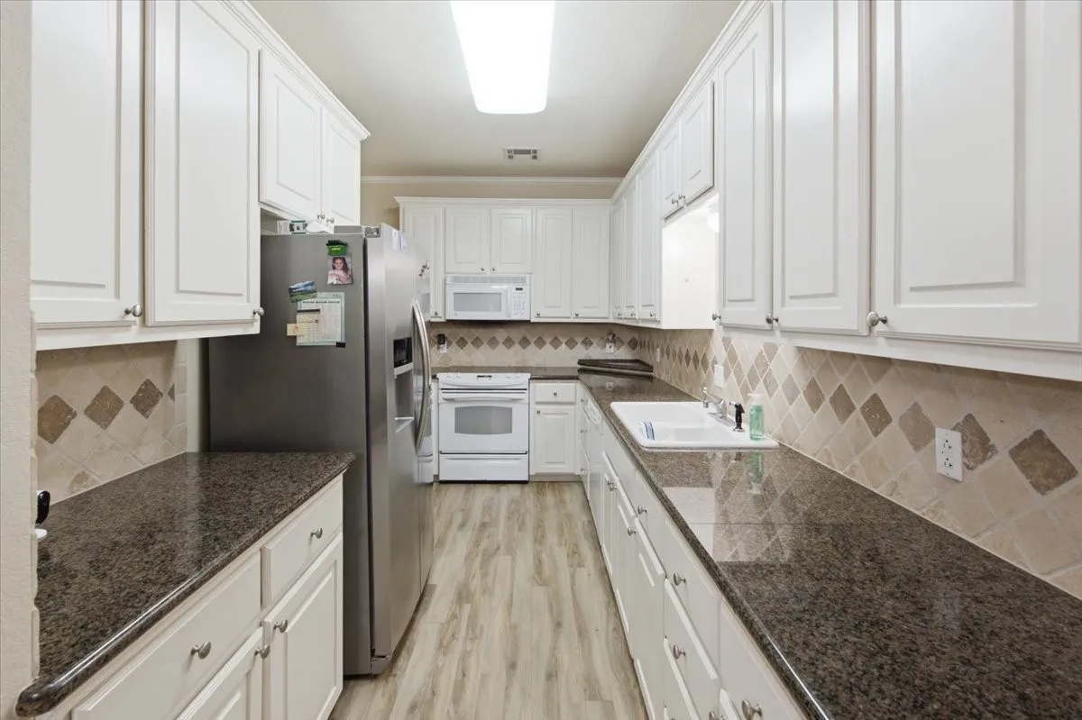 Galley kitchen featuring extensive white cabinetry, dark stone countertops, tile backsplash with diamond accents, and wood-finish flooring
