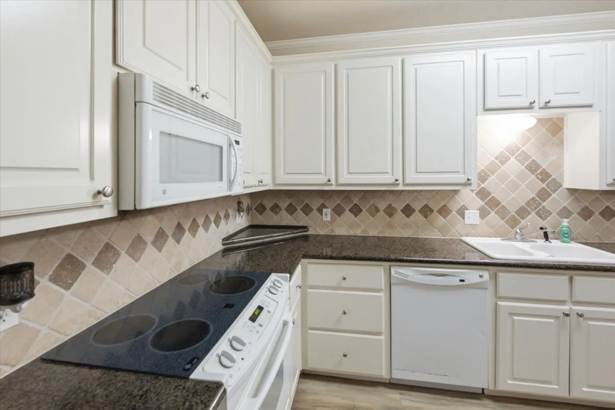 Kitchen featuring white cabinetry, dark countertops, a built-in microwave, integrated electric oven and cooktop, and a tile backsplash