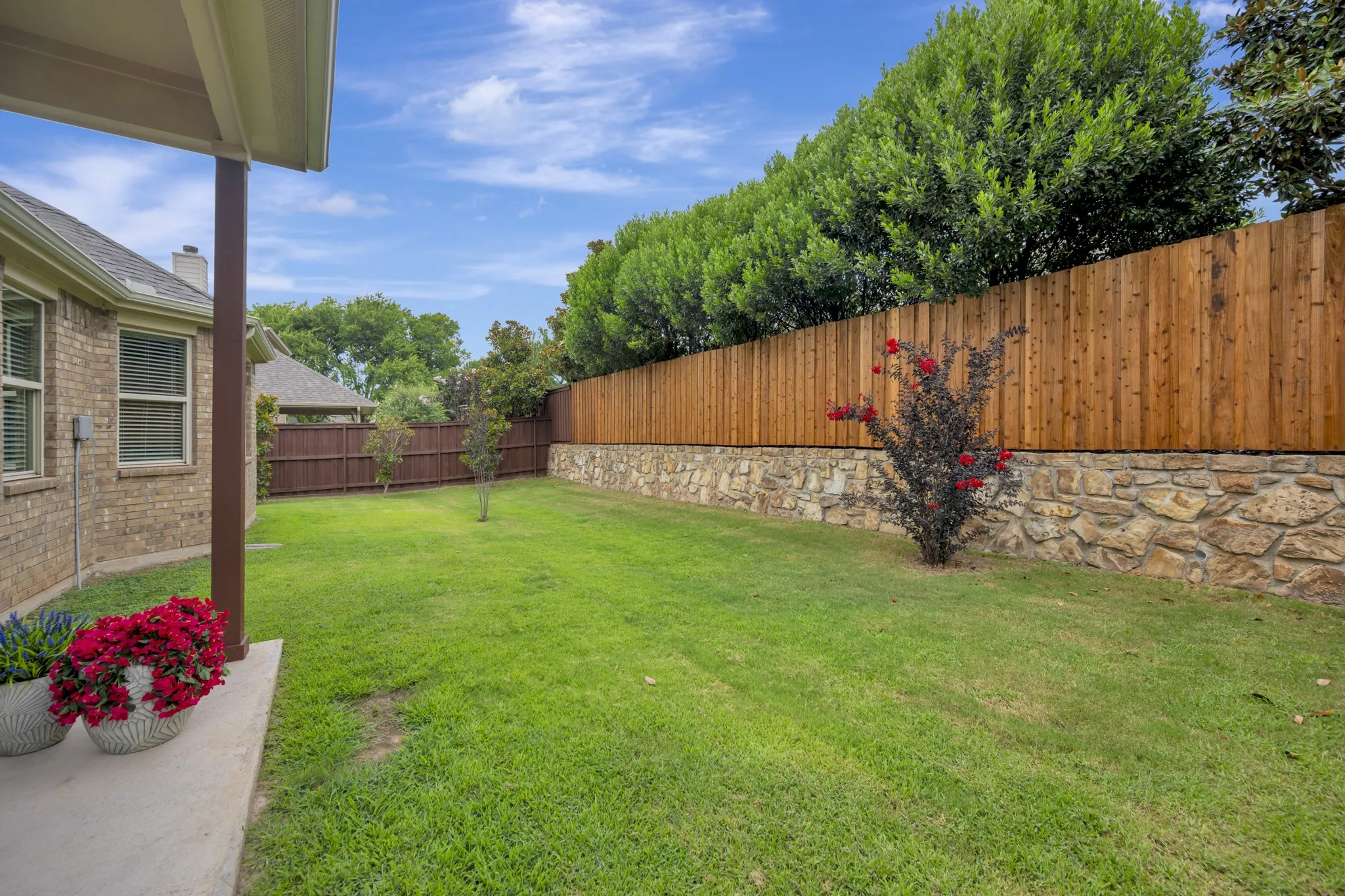 Expansive backyard featuring a lush lawn, a stone retaining wall, and a wood privacy fence