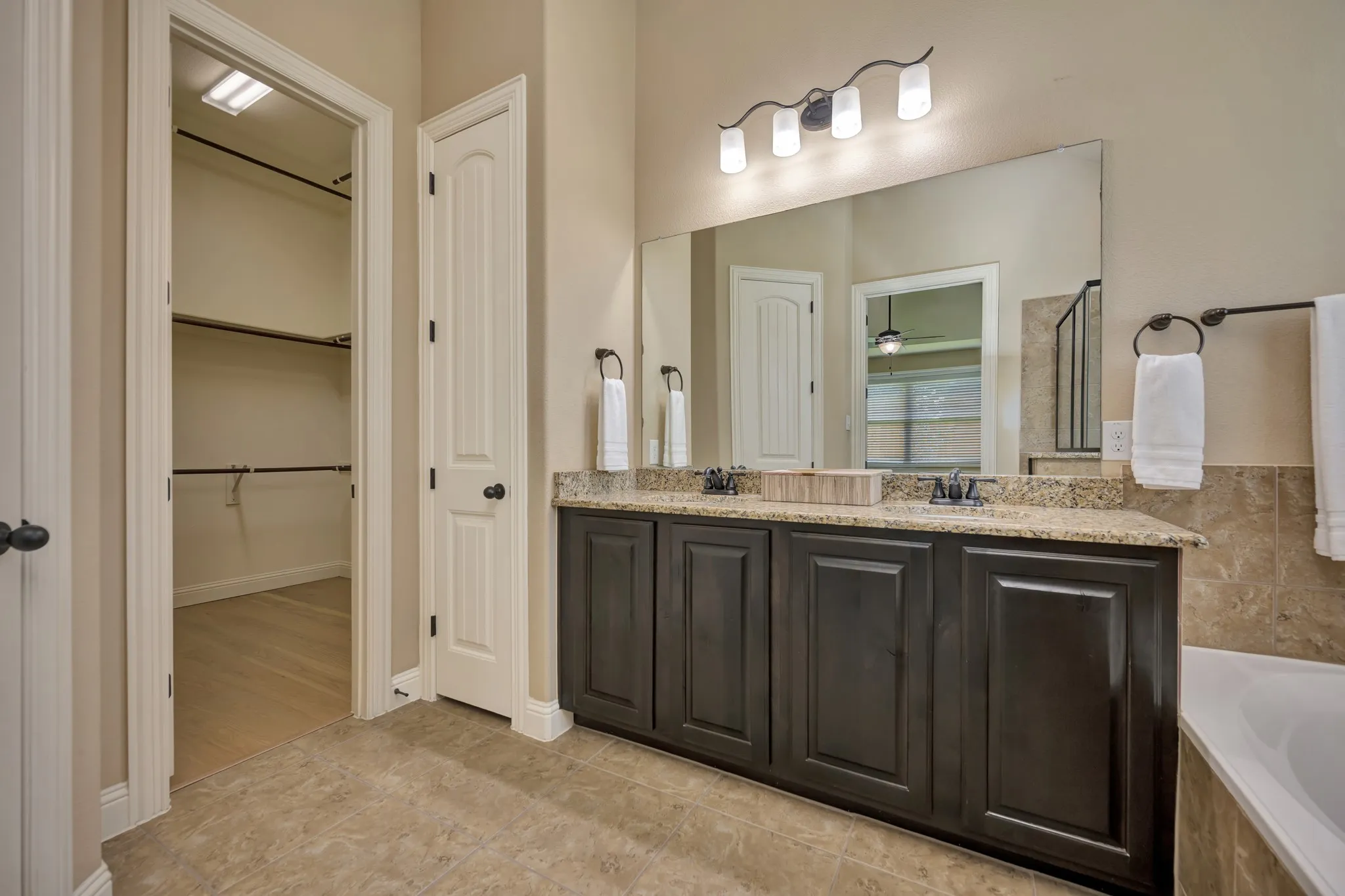 Bathroom featuring a dual-sink vanity with a granite countertop, dark wood cabinetry, and a full-width mirror