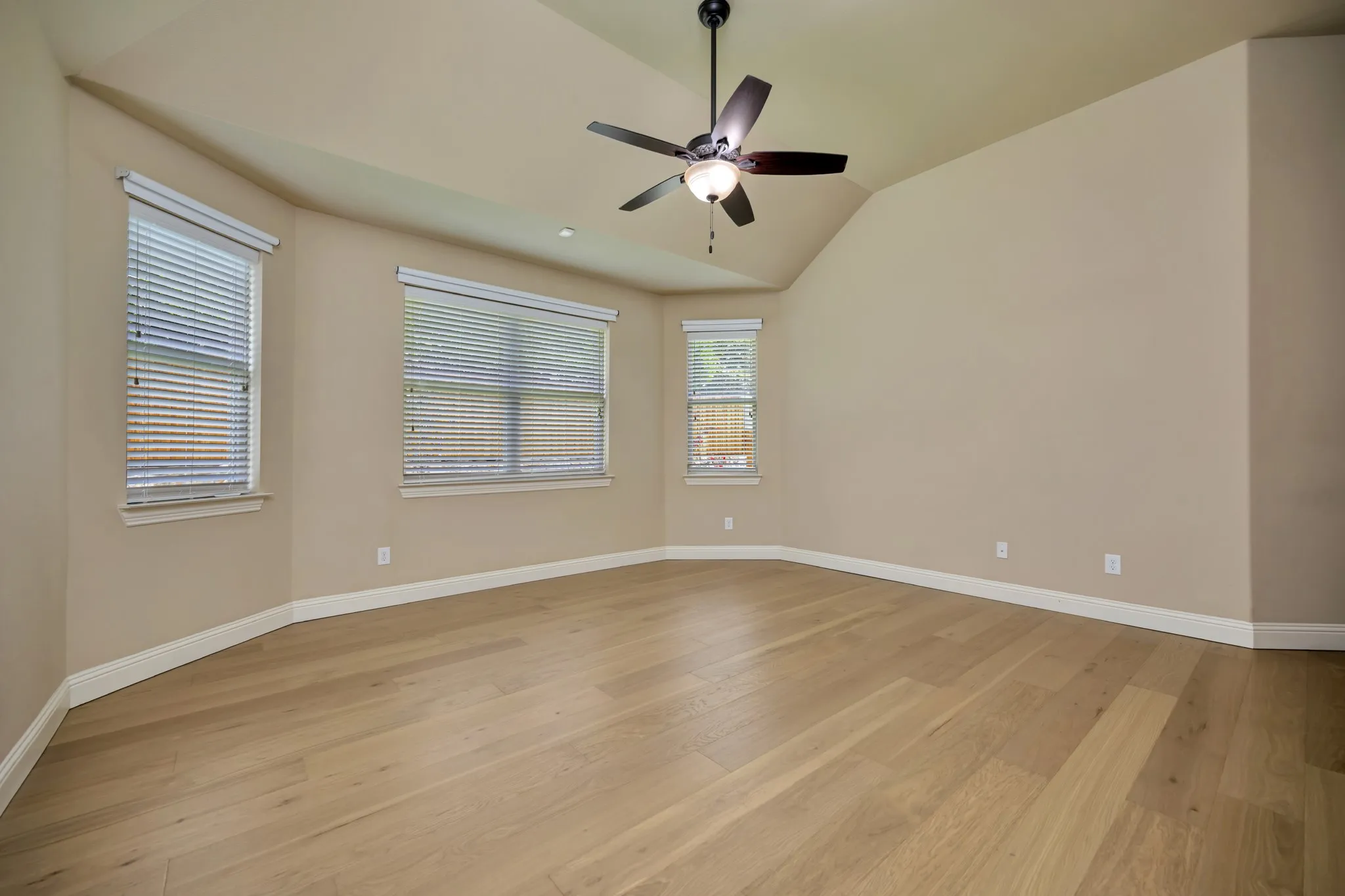 Vaulted ceiling room featuring wood-finish flooring, multiple windows, and a ceiling fan with integrated lighting