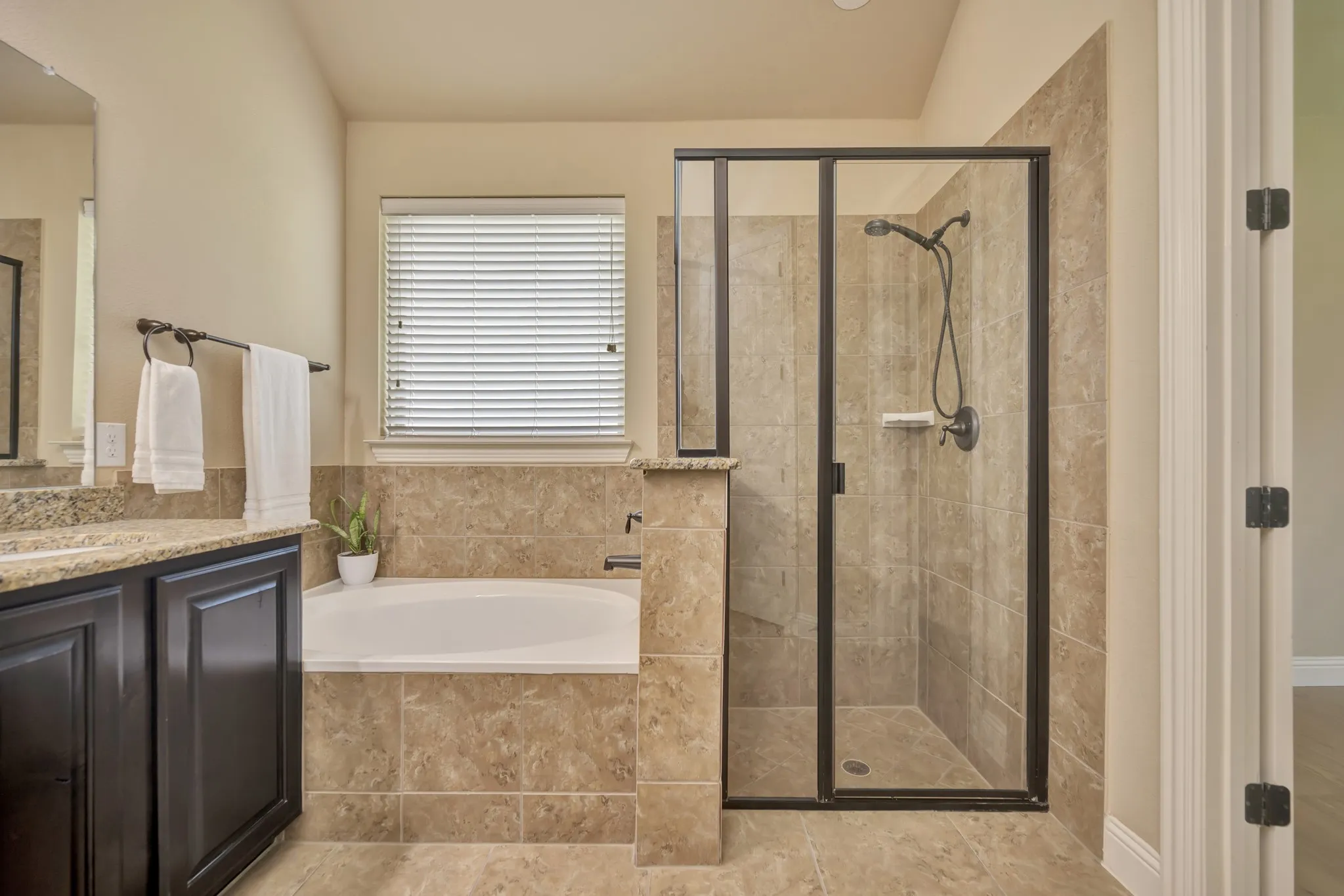 Bathroom featuring a built-in soaking tub, a tiled shower enclosure with a glass door, a vanity with dark wood cabinetry, and a light-toned countertop
