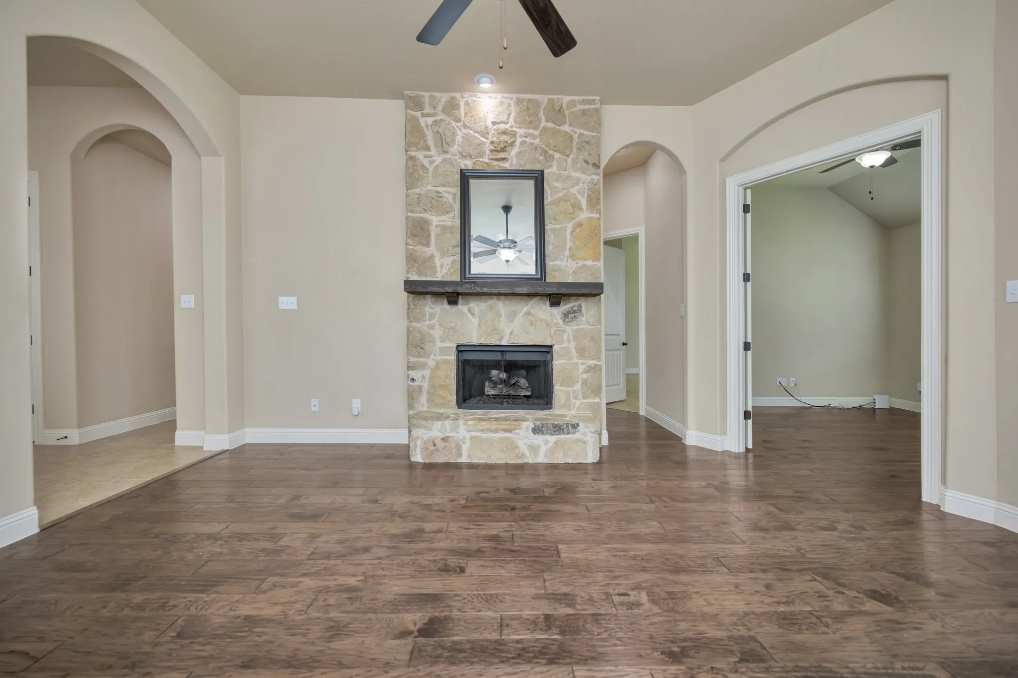 Living space featuring a stone fireplace with a wood-finish mantel, wood-finish flooring, and arched doorways