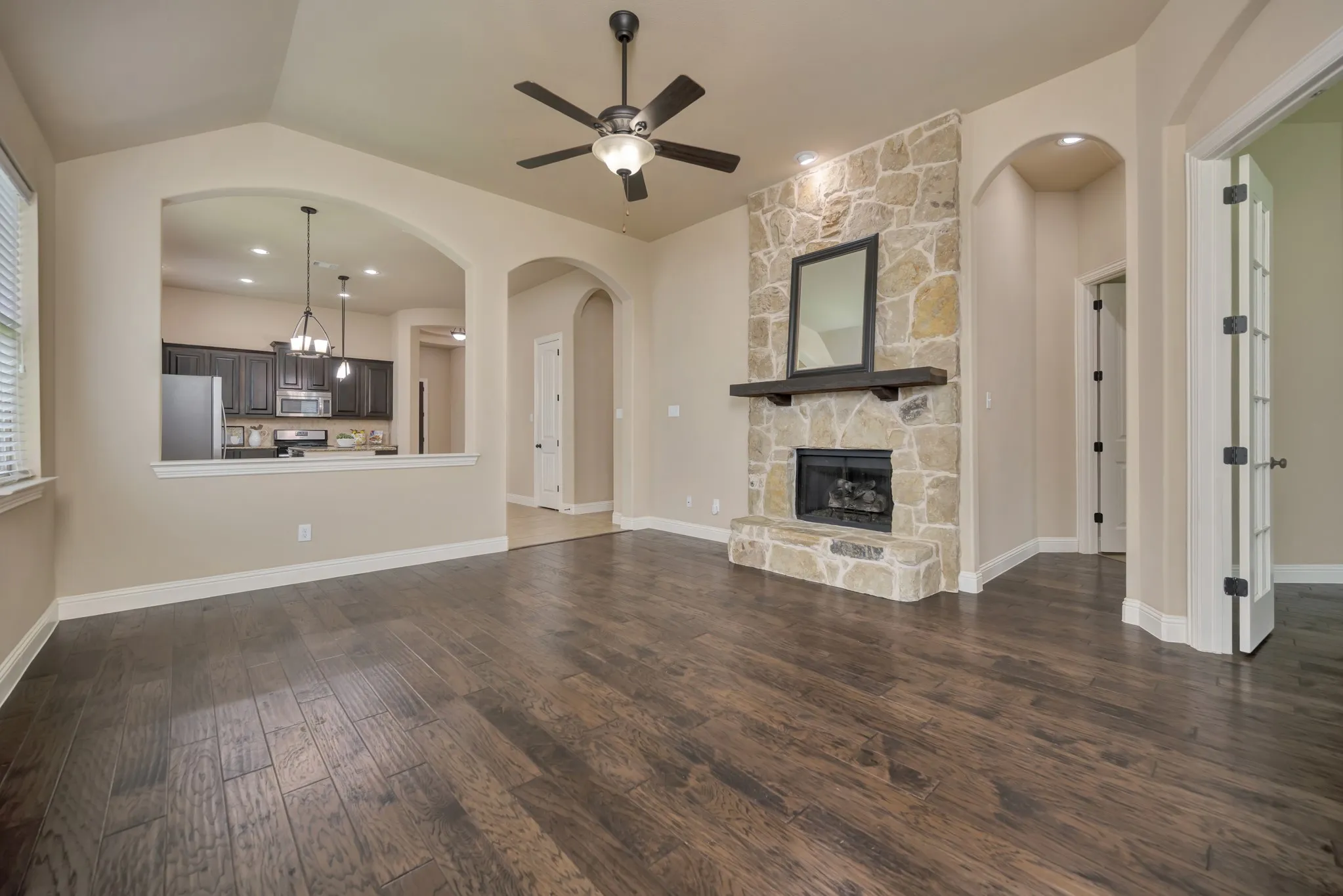 Living area featuring a stone fireplace with a dark wood mantel, wood-finish flooring, and an archway opening to the kitchen