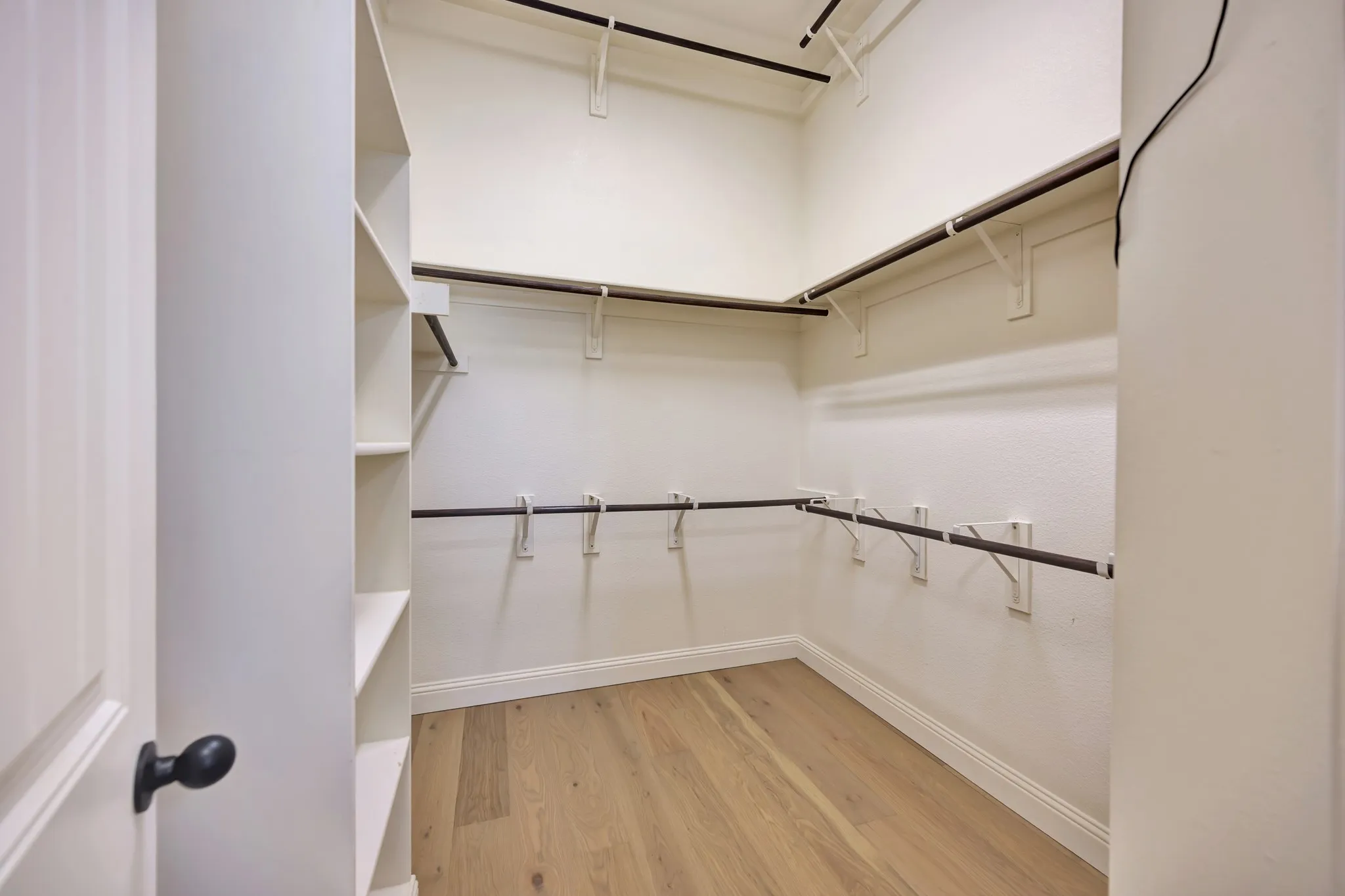 Walk-in closet featuring wood-finish flooring, built-in shelving, multiple hanging rods, and white baseboards