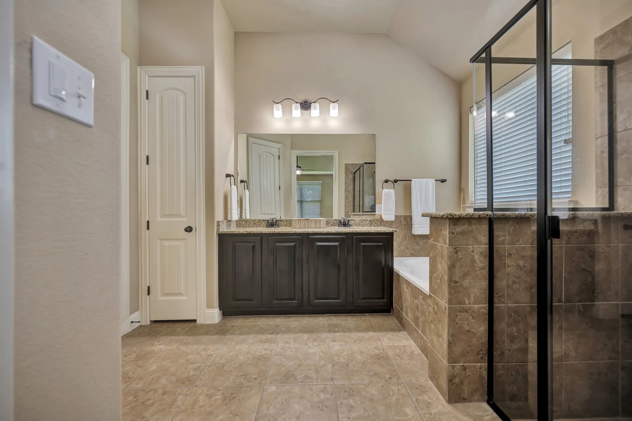 Bathroom featuring a double vanity with stone-finish countertop, dark wood-finish cabinetry, and framed mirror
