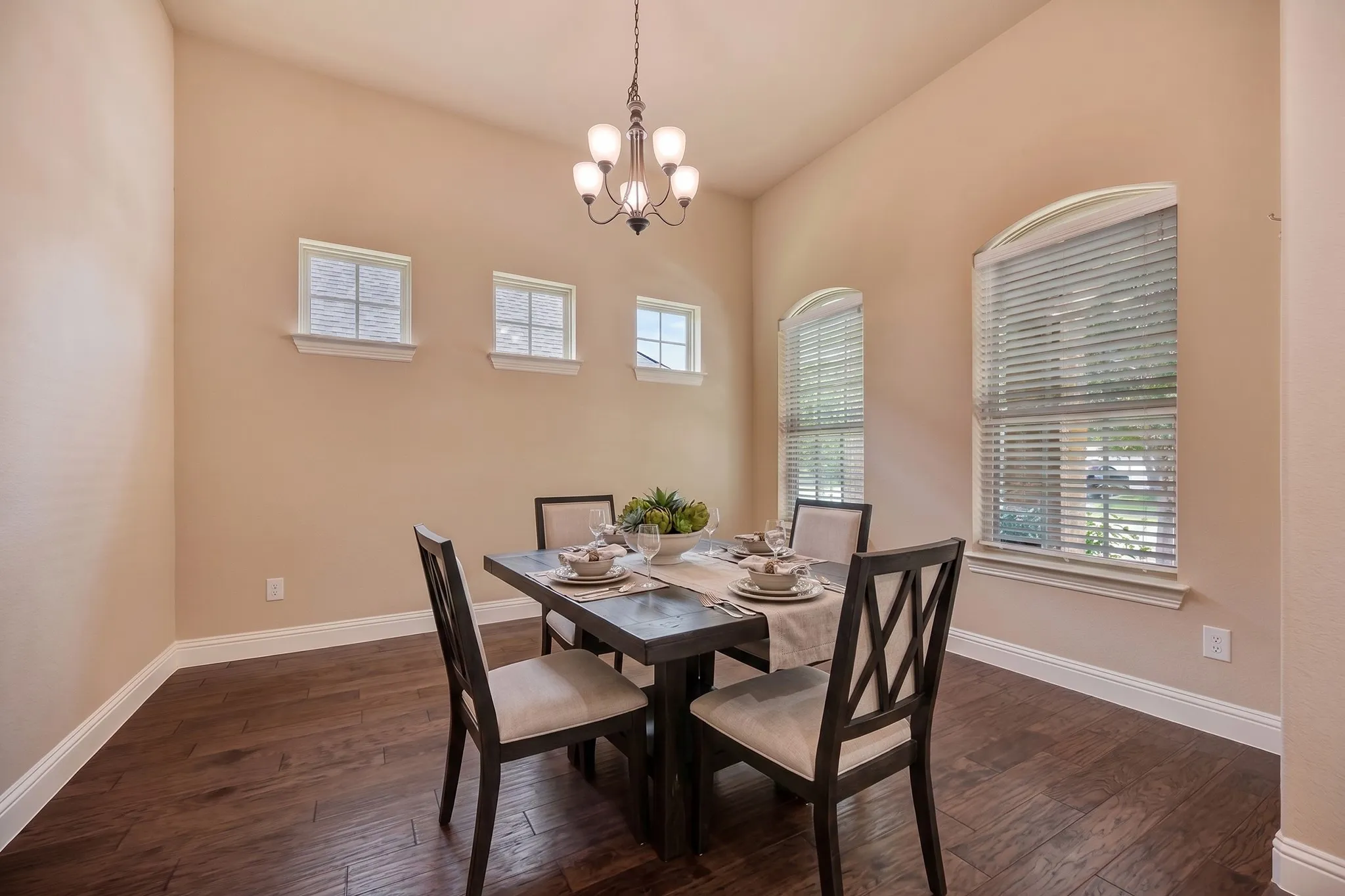 Dining area featuring wood-finish flooring, high ceilings, multiple window styles, and a ceiling-mounted chandelier