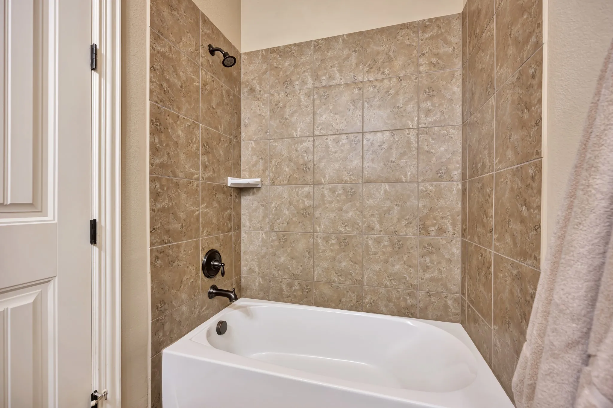 White soaking tub with oil-rubbed bronze fixtures and a tiled shower surround