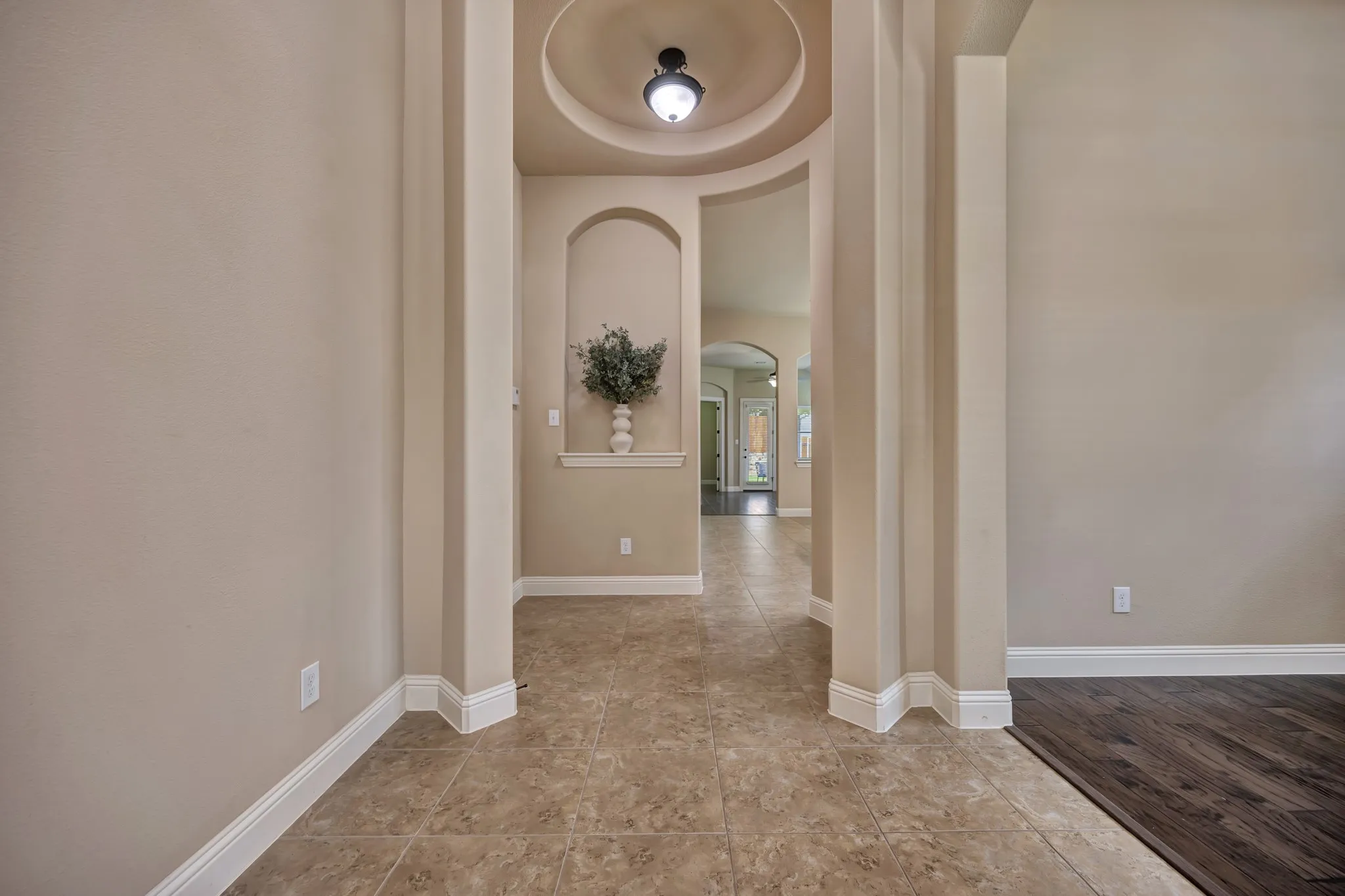 Arched entryway featuring a recessed ceiling with a flush-mount light fixture, a built-in display niche, and tile flooring