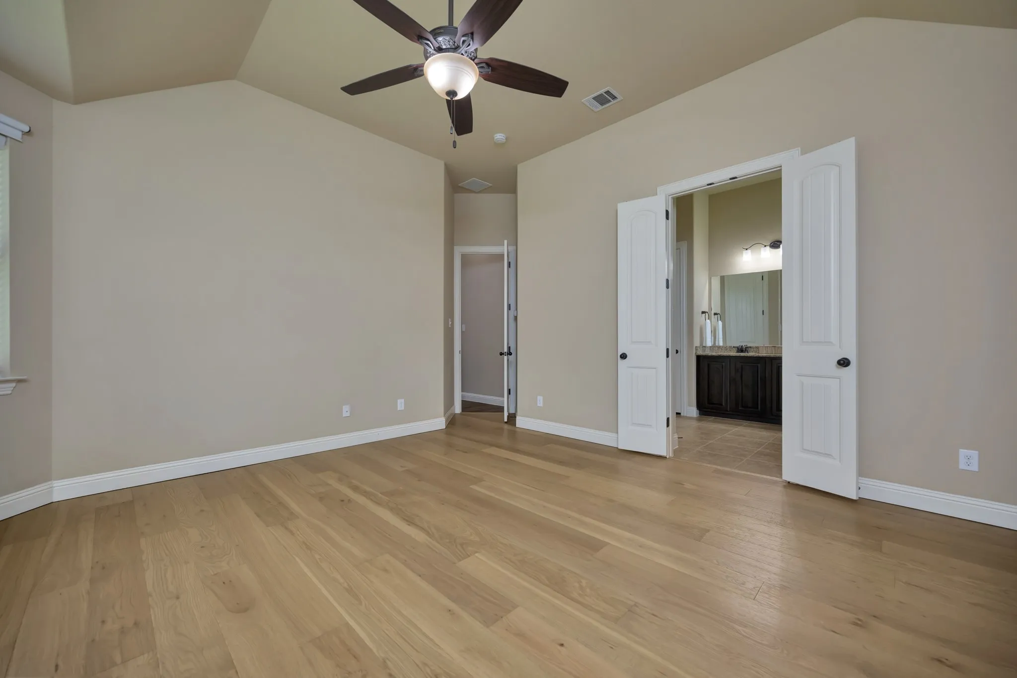 Spacious room featuring vaulted ceilings, wood-finish flooring, a ceiling fan with integrated lighting, and white baseboards