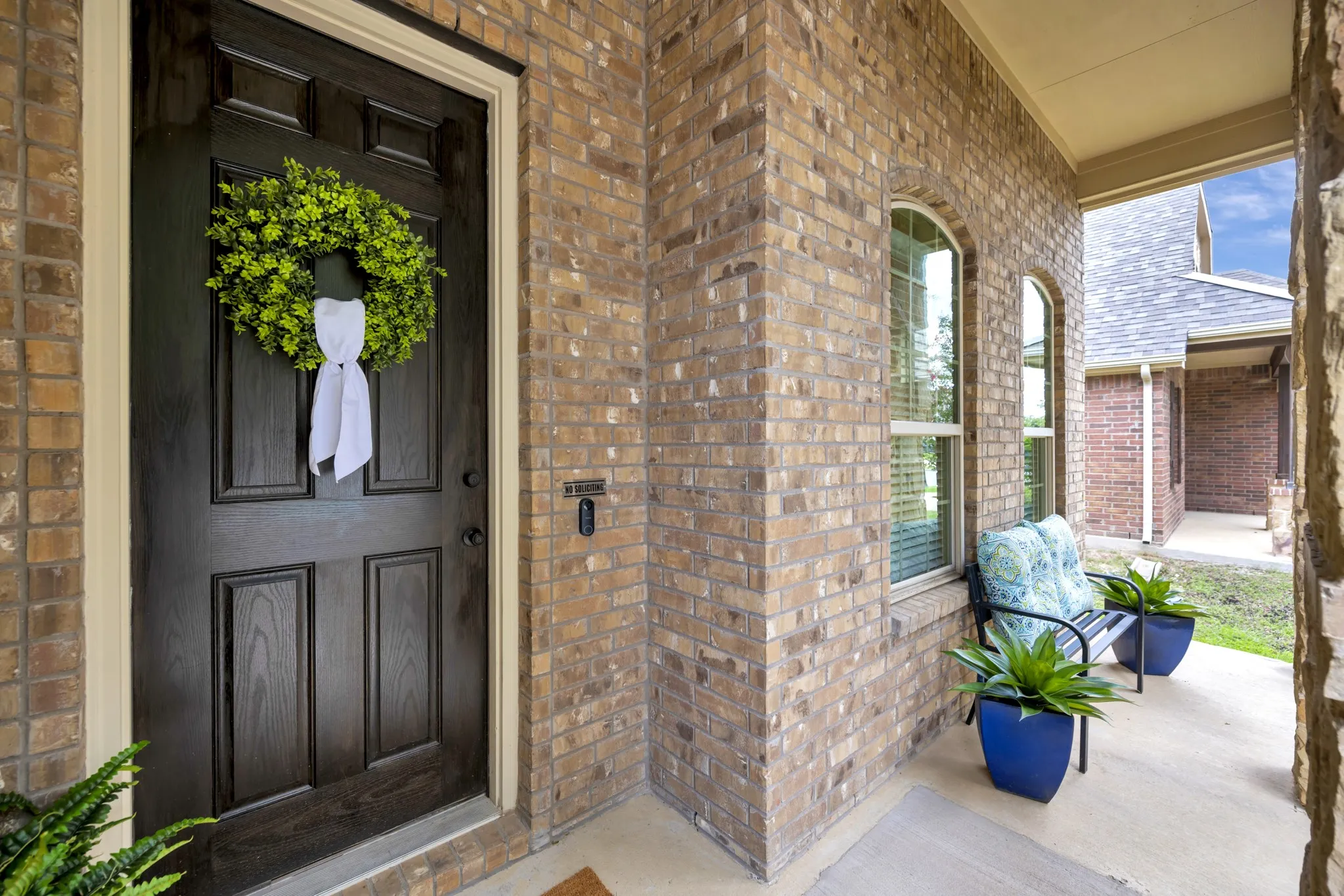 Front entry featuring a paneled dark wood door, brick facade, arched windows, covered porch, and concrete flooring